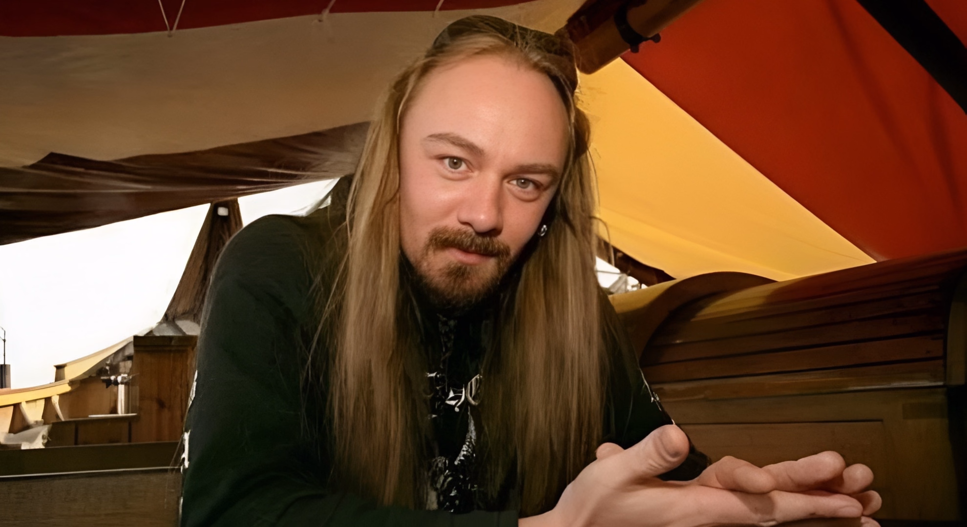 ‘Scandinavian Metal Attack’ Gave Thor to Bathory First Quorthon of Bathory, long-haired and in a black shirt, leans on a wooden chest aboard a replica Viking ship beneath a red and yellow sail.