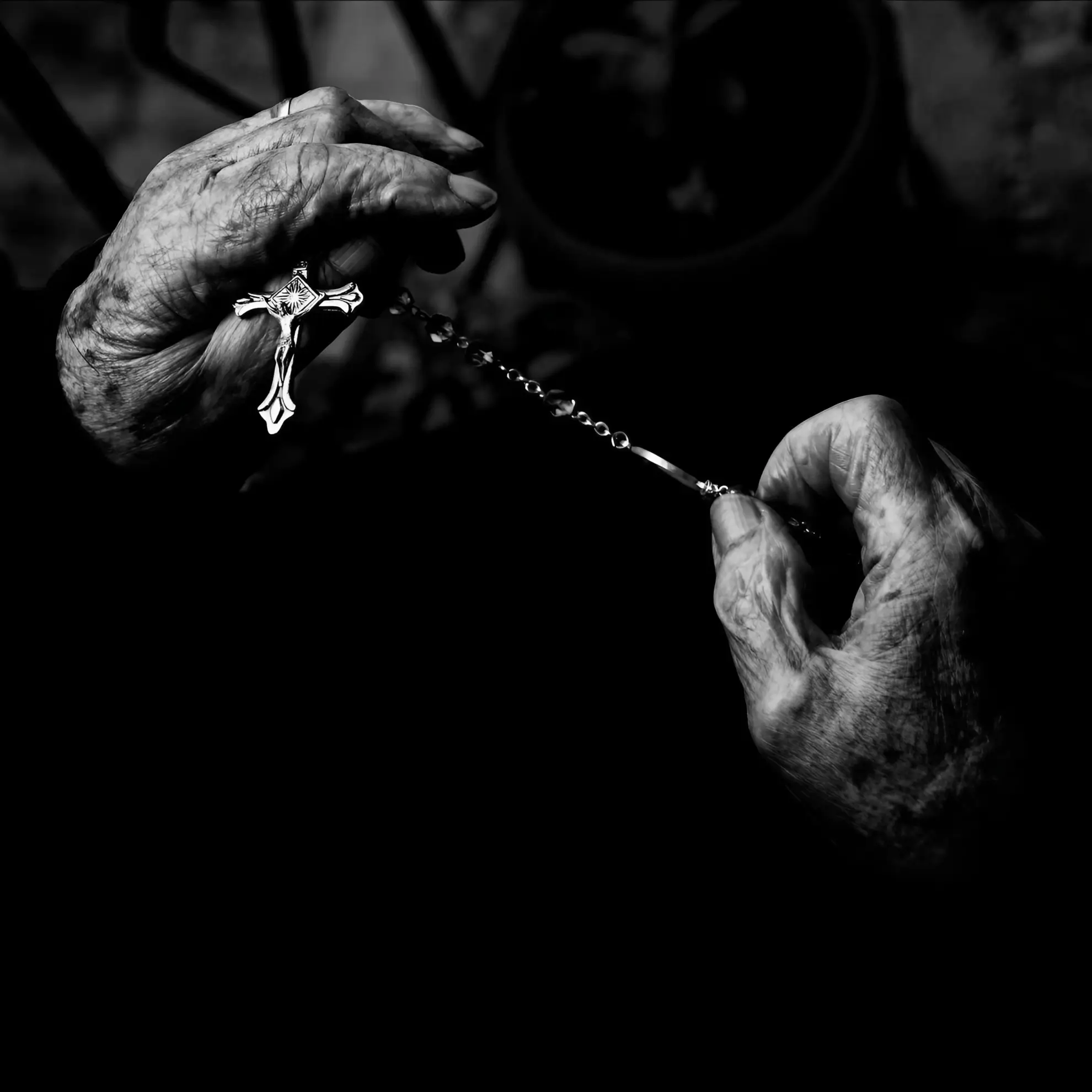 Elderly hands holding a rosary with a crucifix, in high-contrast black and white, for the album ‘Għadam’ by Maltese band Beheaded.