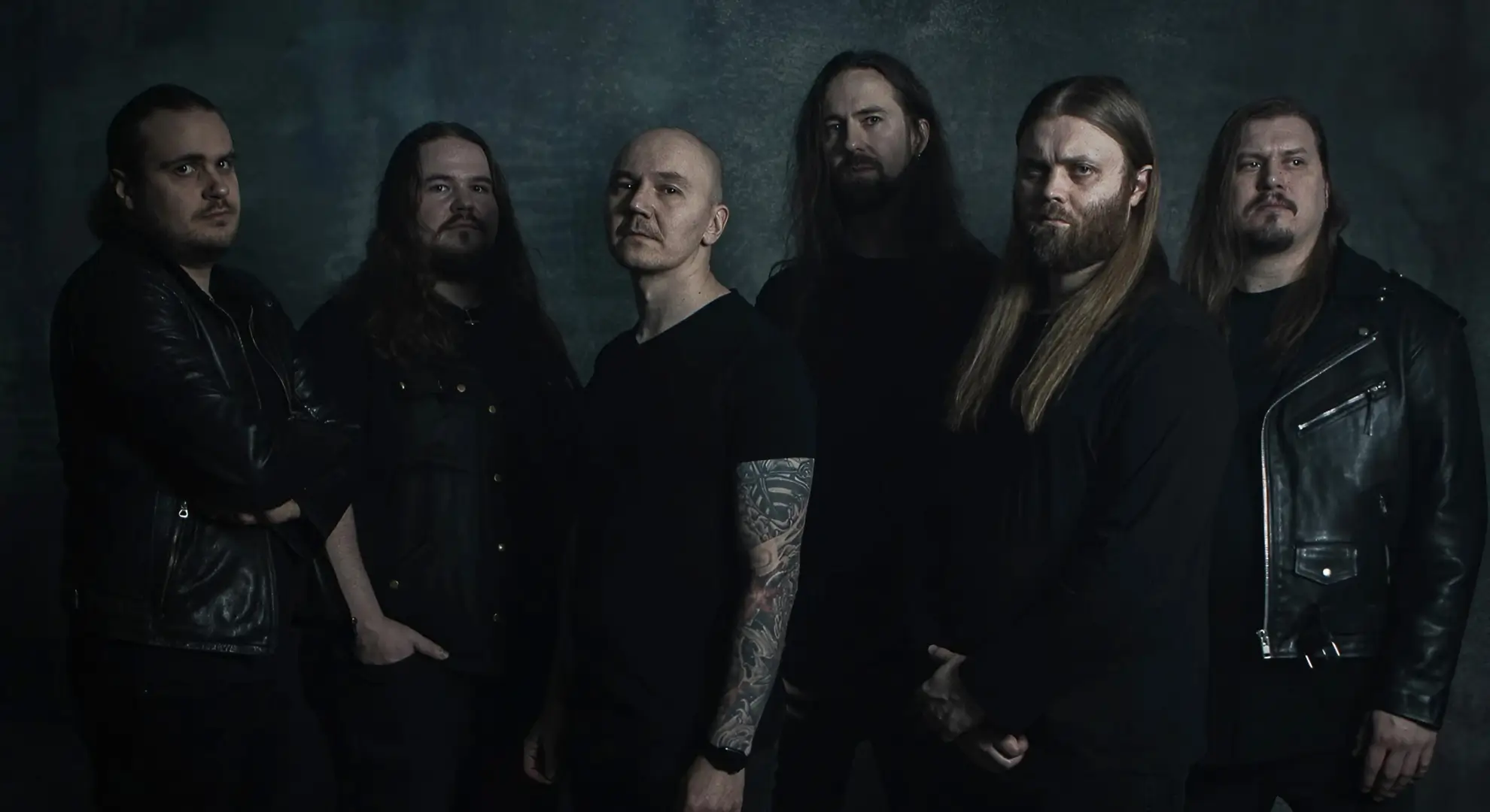 All six members of Slow Fall standing against a dark textured backdrop, wearing black clothing and facing the camera.