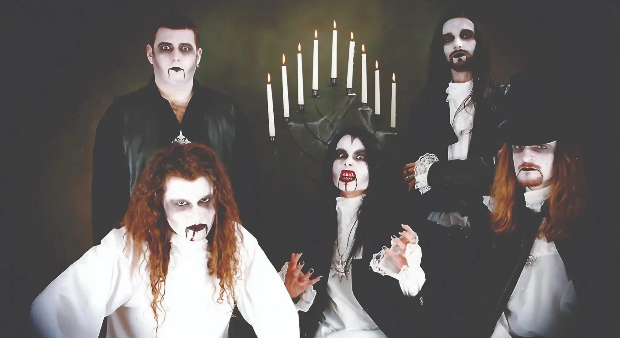 Cradle of Filth posed in gothic, vampire-style attire and makeup in front of a candelabra.
