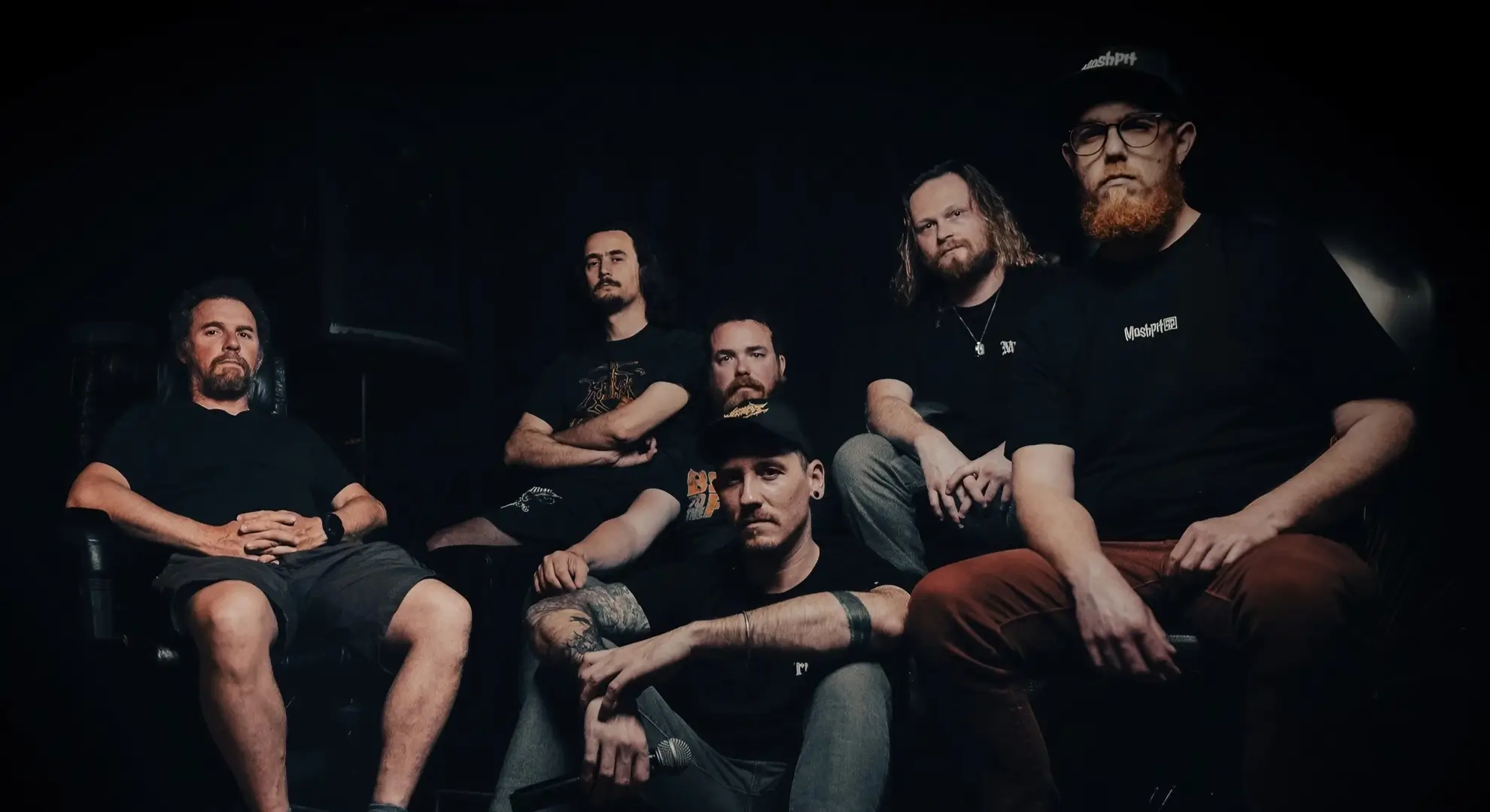 A group photo of the French metal band Horror Within. The six members are seated in a dimly lit, dark room, looking seriously toward the camera.