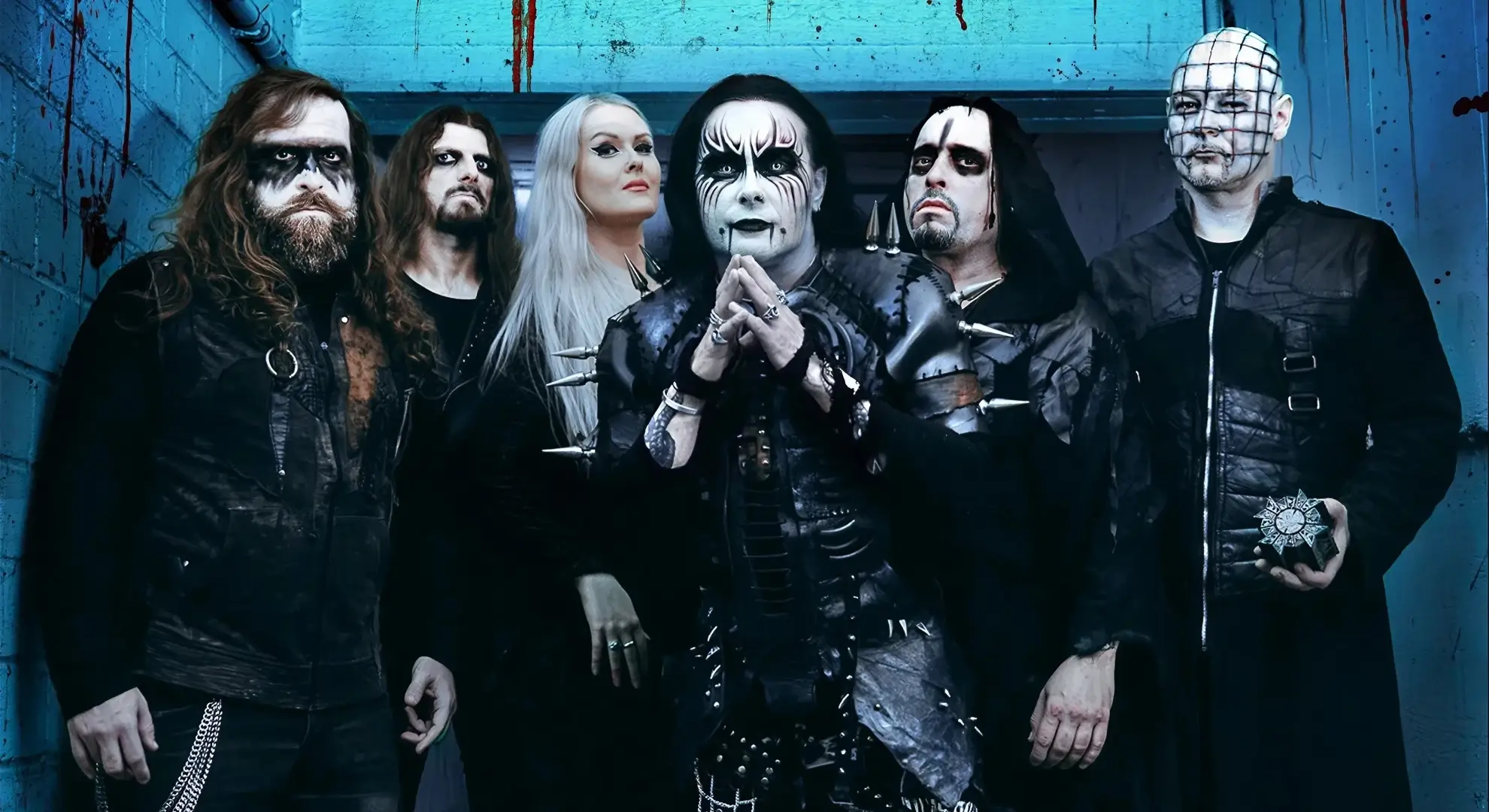 The members of Cradle of Filth in full stage makeup and costume, standing in a corridor with blood-spattered walls.