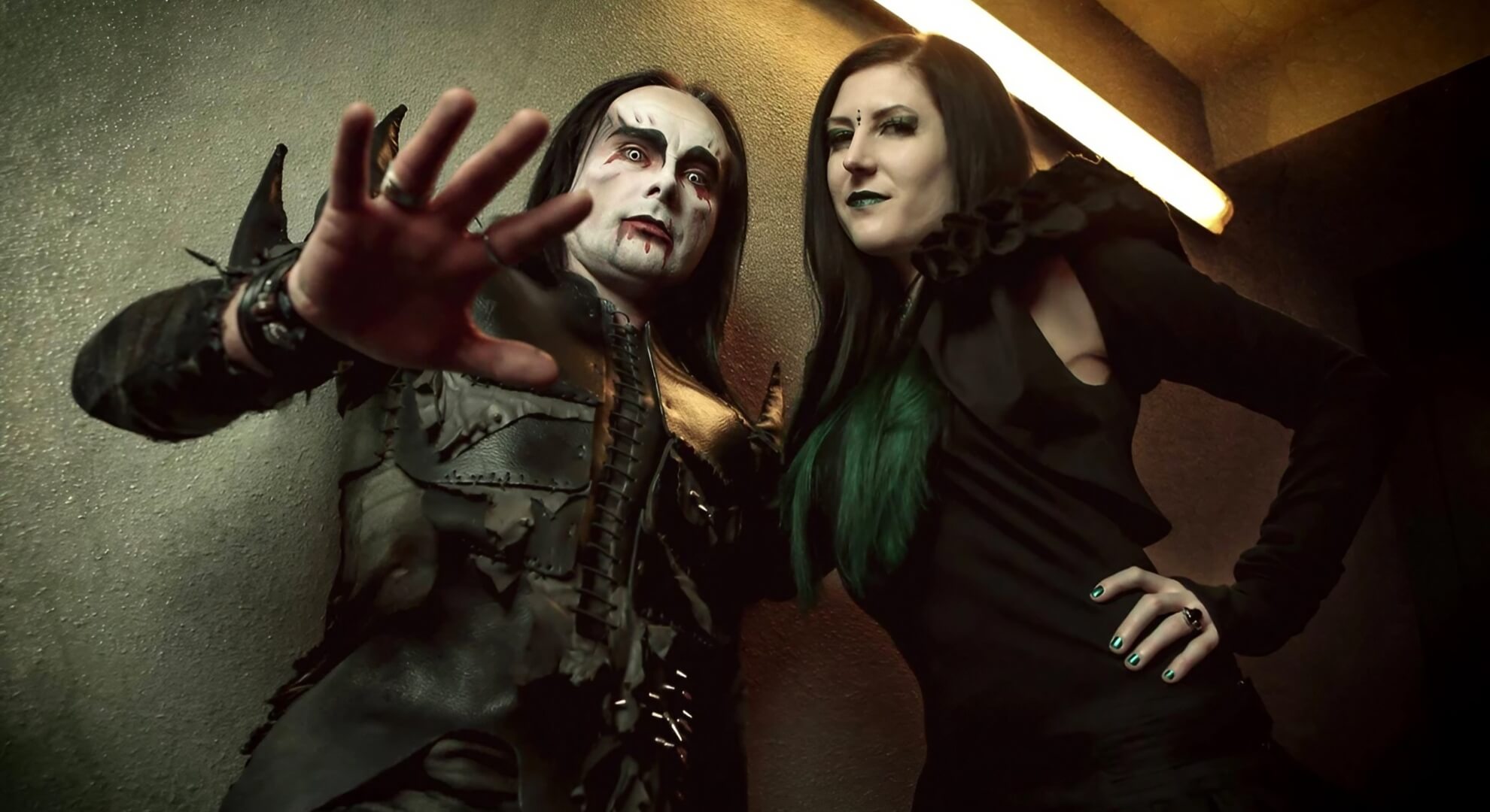 Daniel Davey and Lindsay Schoolcraft of Cradle of Filth, with Davey in stage makeup raising a hand.