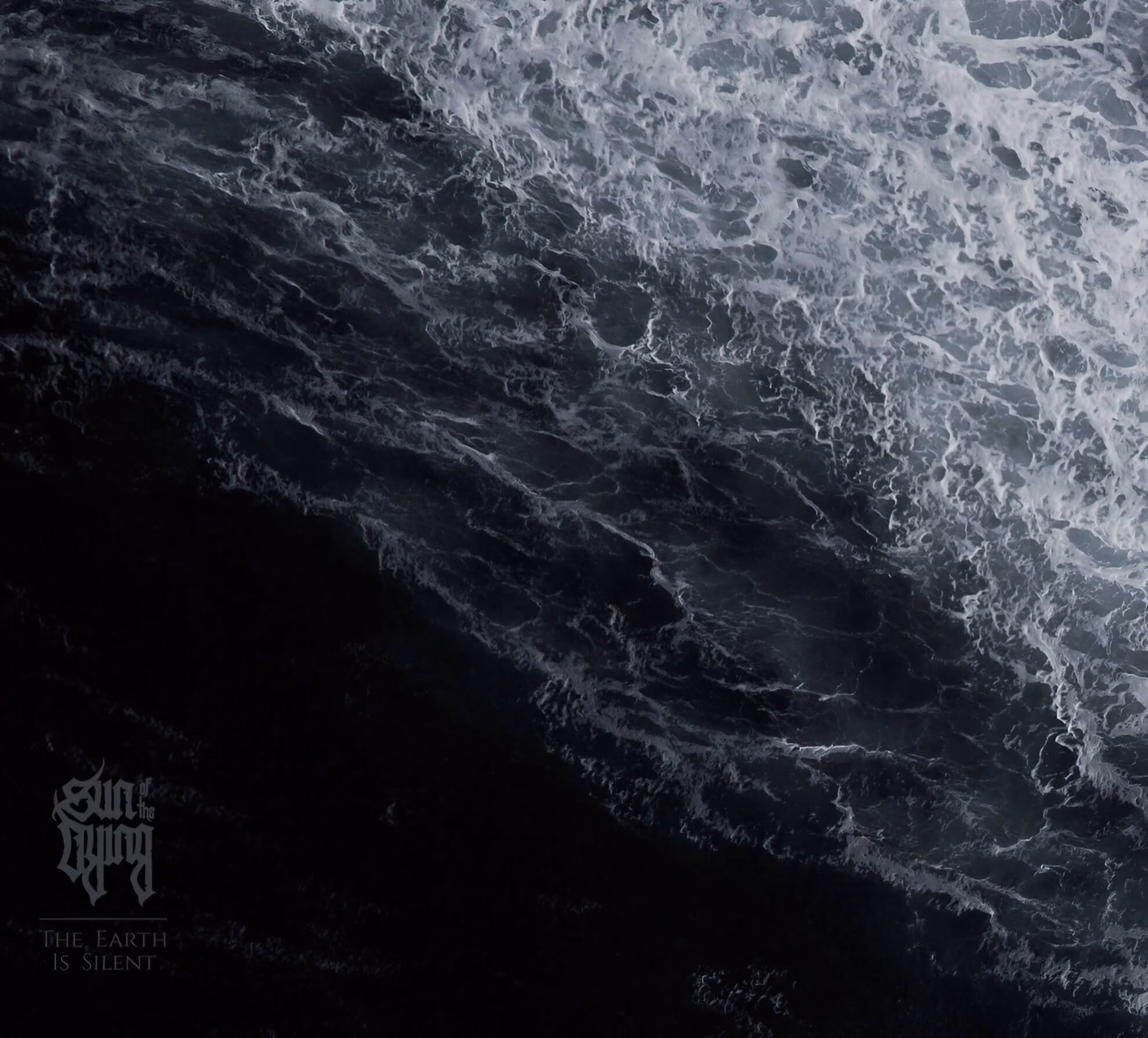 The album cover for &lsquo;The Earth Is Silent.&rsquo; A monochromatic, high-contrast, top-down view of dark, turbulent water with white foam. The band&rsquo;s logo and album title are in the lower-left corner.