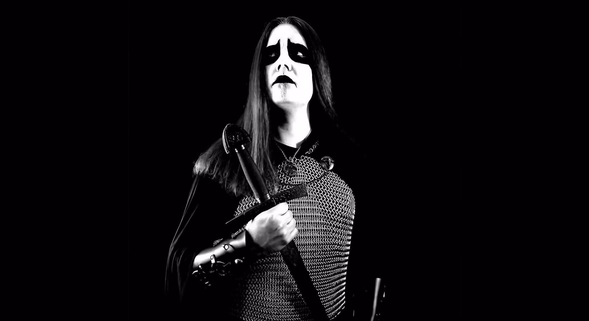 A musician in corpsepaint and chainmail holds a sword against a black background.