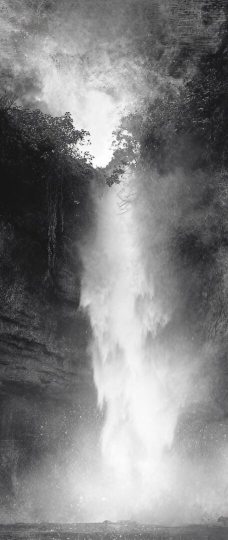 A black and white, atmospheric image of a powerful waterfall cascading down a dark, rocky cliff surrounded by dense foliage.