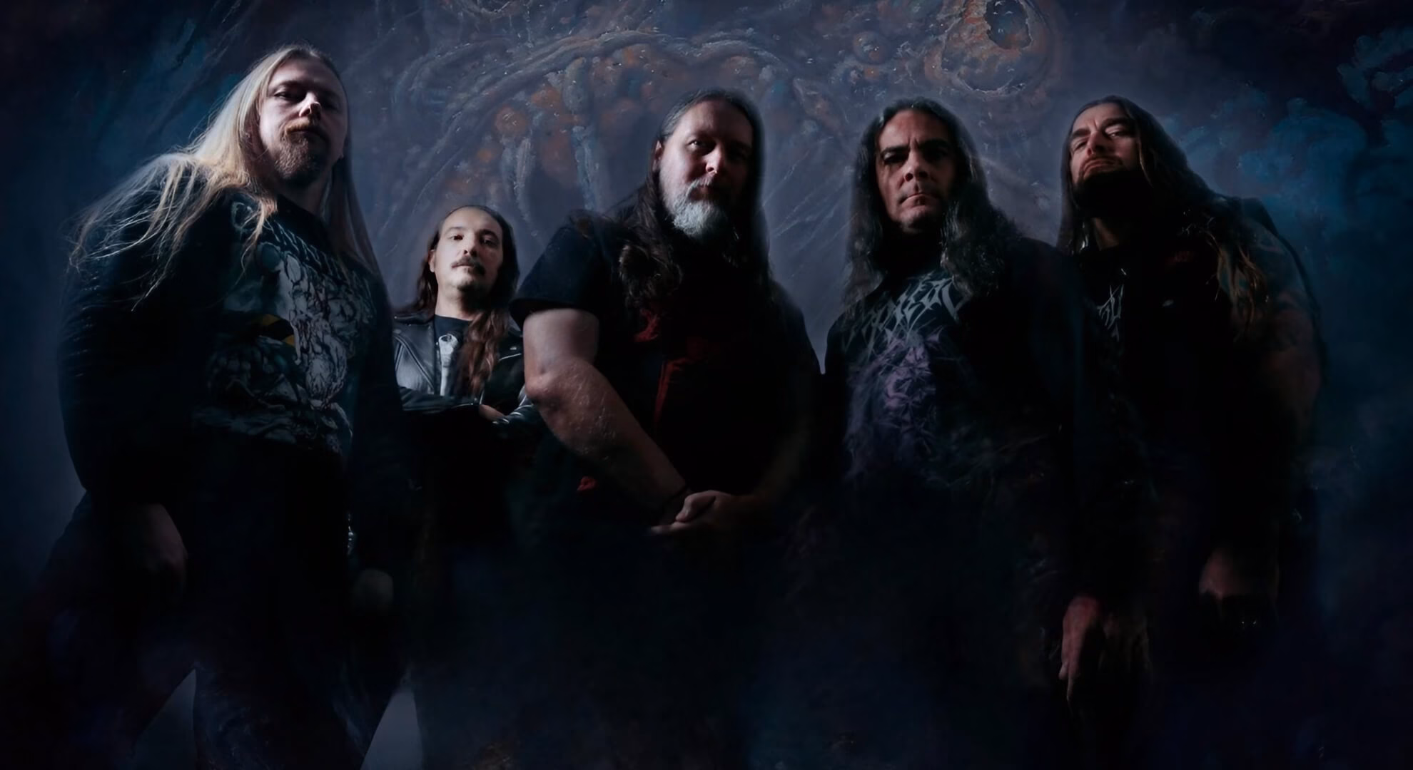 A low-angle shot of the five-piece band Depravity posed before a dark, painted, monstrous backdrop.