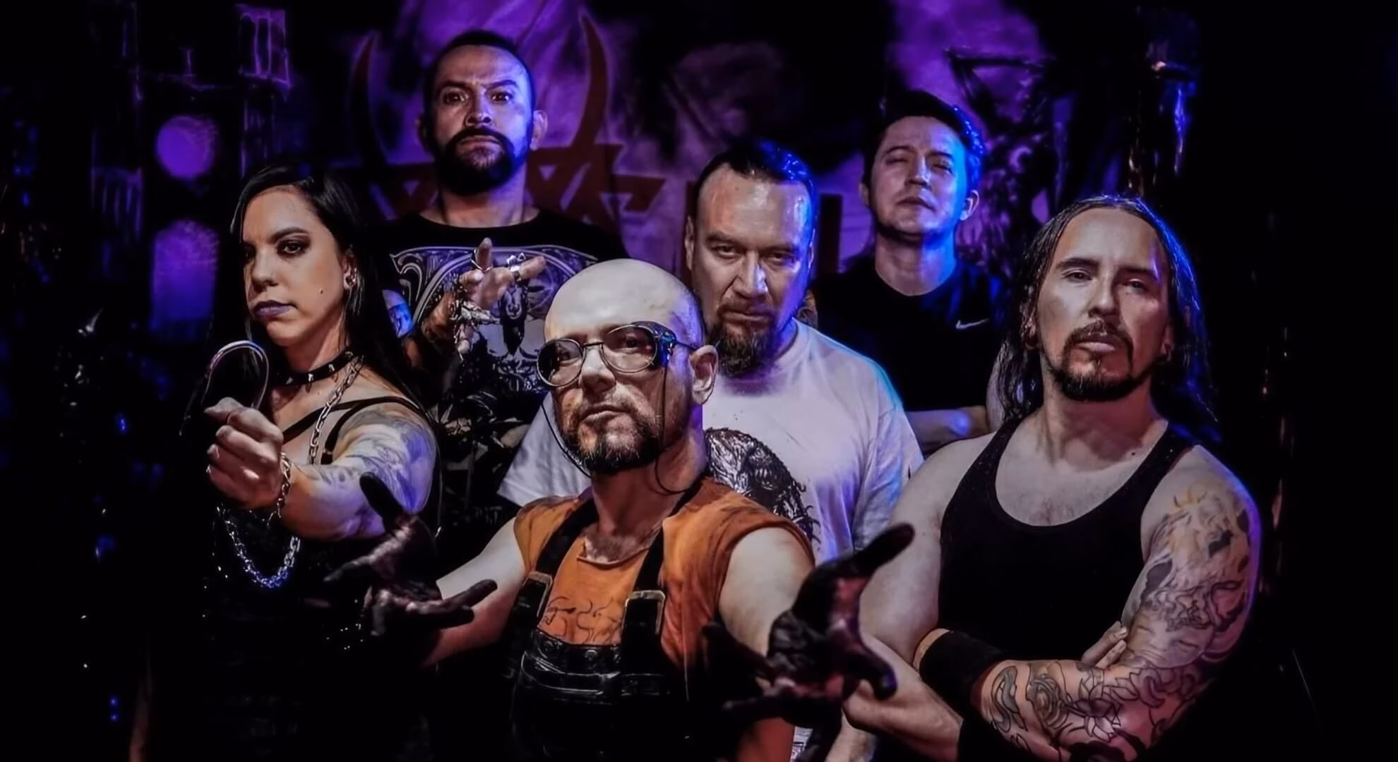 The six members of Vein pose in a dark, dramatically lit space. Painter Iván Chacón is in front, hands outstretched.