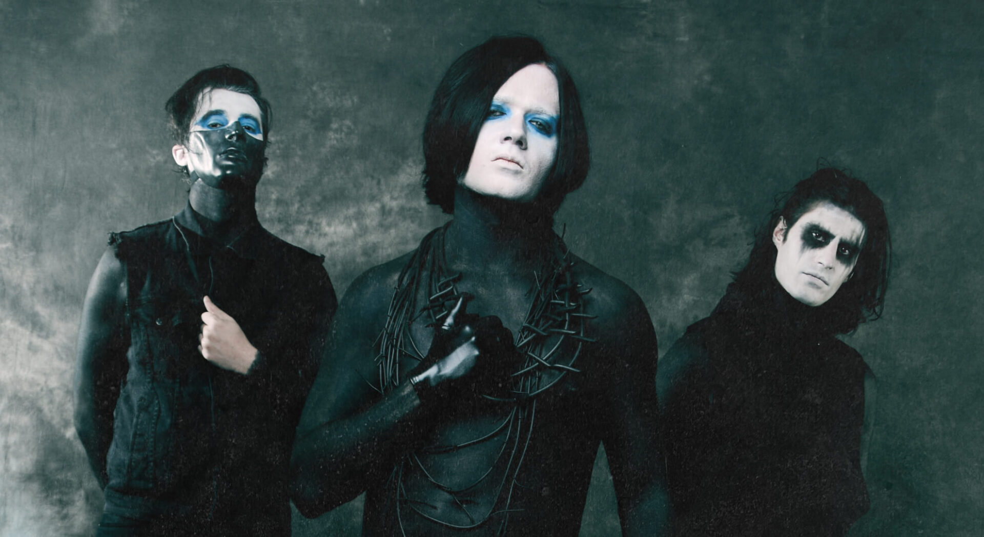 Heartlay’s three members in black clothing with white, black, and blue face makeup against a dark grey backdrop.