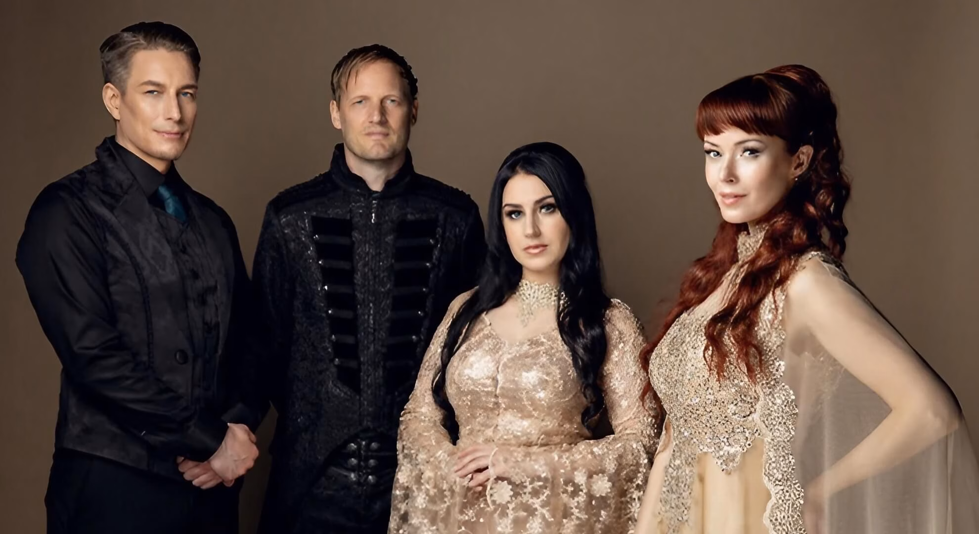 Two men in dark formal jackets and two women in flowing gold gowns stand together against a neutral studio background.
