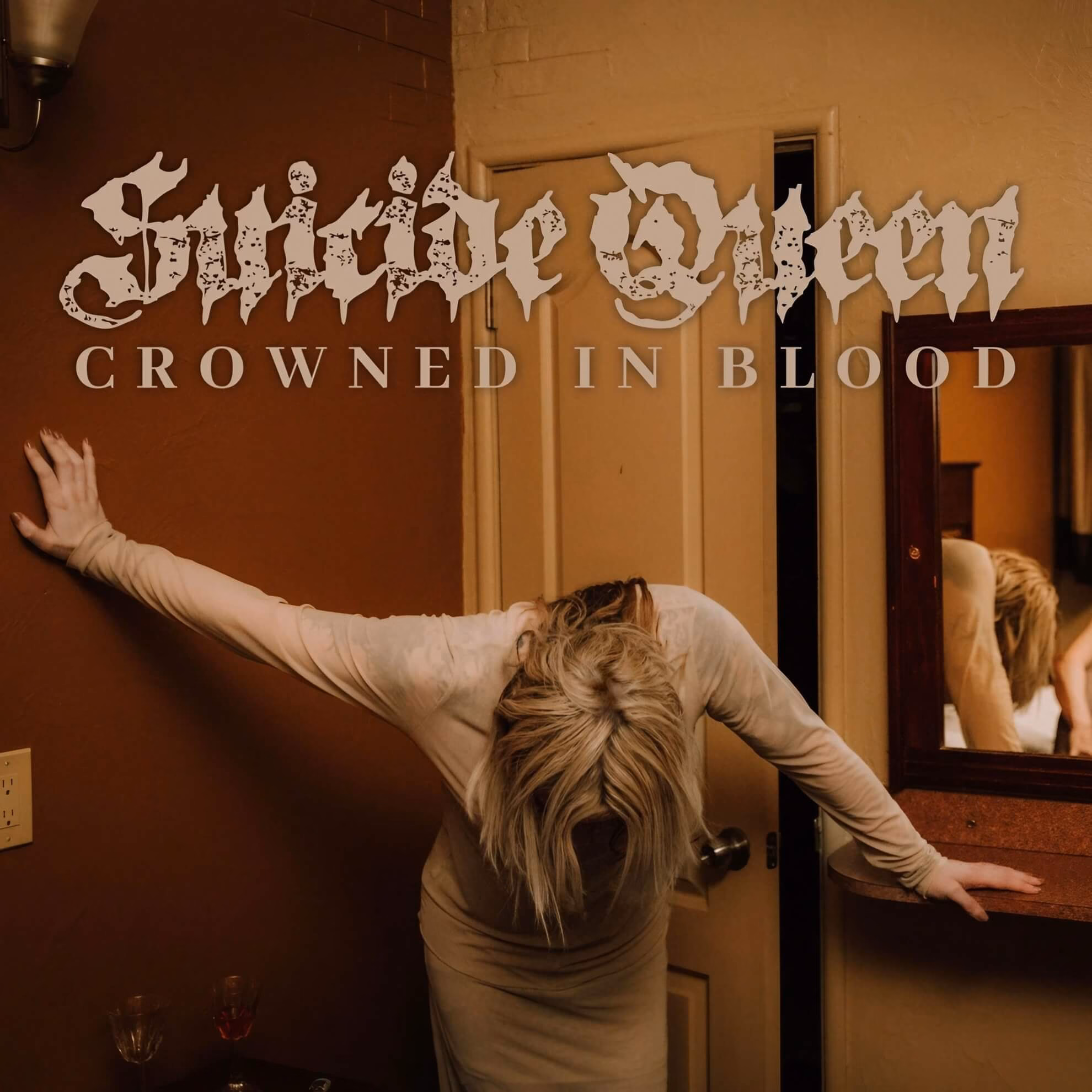 Suicide Queen: The Ritual and Purpose of Pain with ‘Crowned In Blood’ Album cover. A blonde figure in a dress leans forward, arms spread in a dim room. The title ‘Crowned In Blood’ overlays the image.