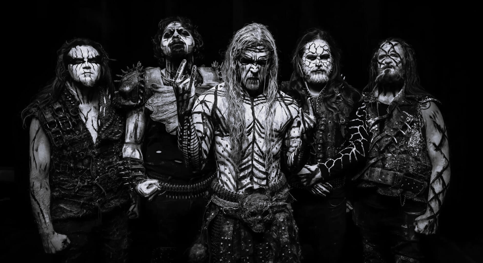 Thy Antichrist band members stand stoically in full ritual body paint and leather armor against a textured, dark gray background.