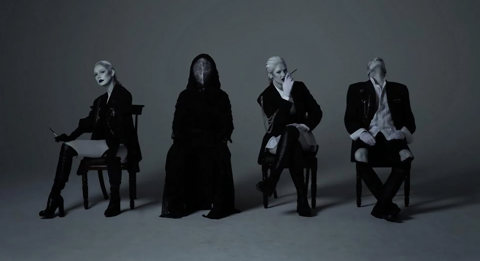 Black Spikes members in pinstripe suits and white makeup pose with a masked figure in a grey studio.