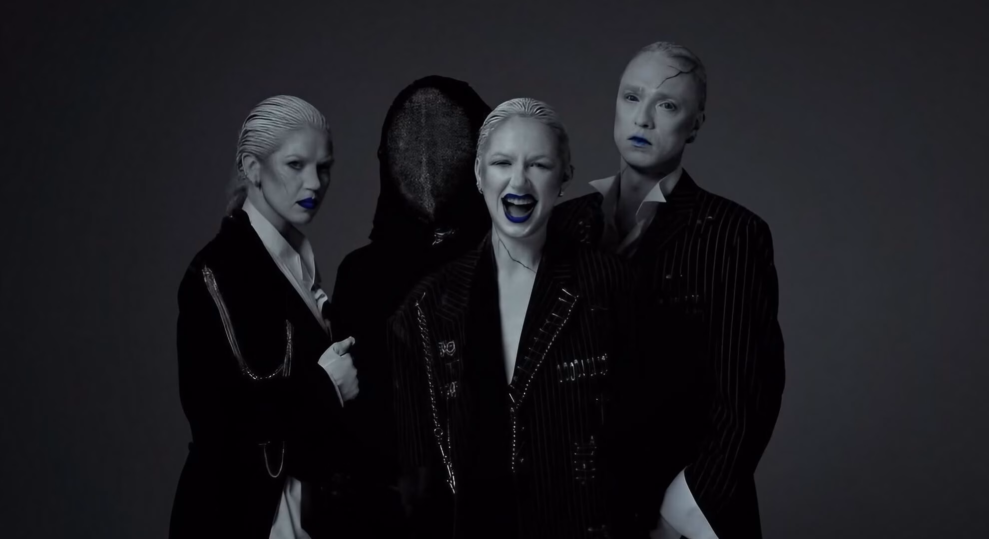 Black Spikes members in deconstructed suits and avantgarde makeup pose with a masked figure against a grey background.