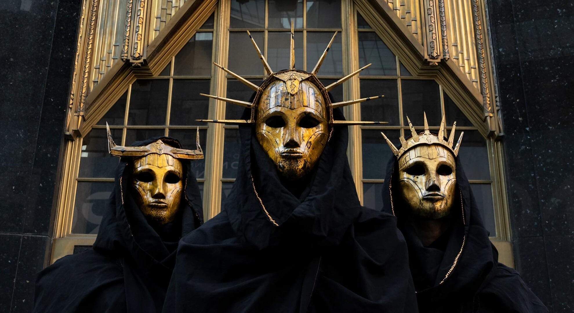 Imperial Triumphant pose in golden Art Deco masks and black robes against an industrial, urban backdrop.