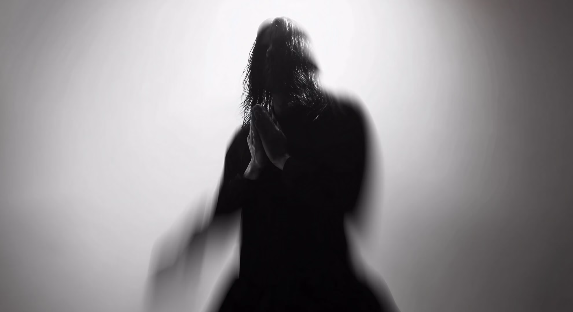 Black and white photograph of a silhouetted figure with long dark, creating an anonymous, ghostly presence.