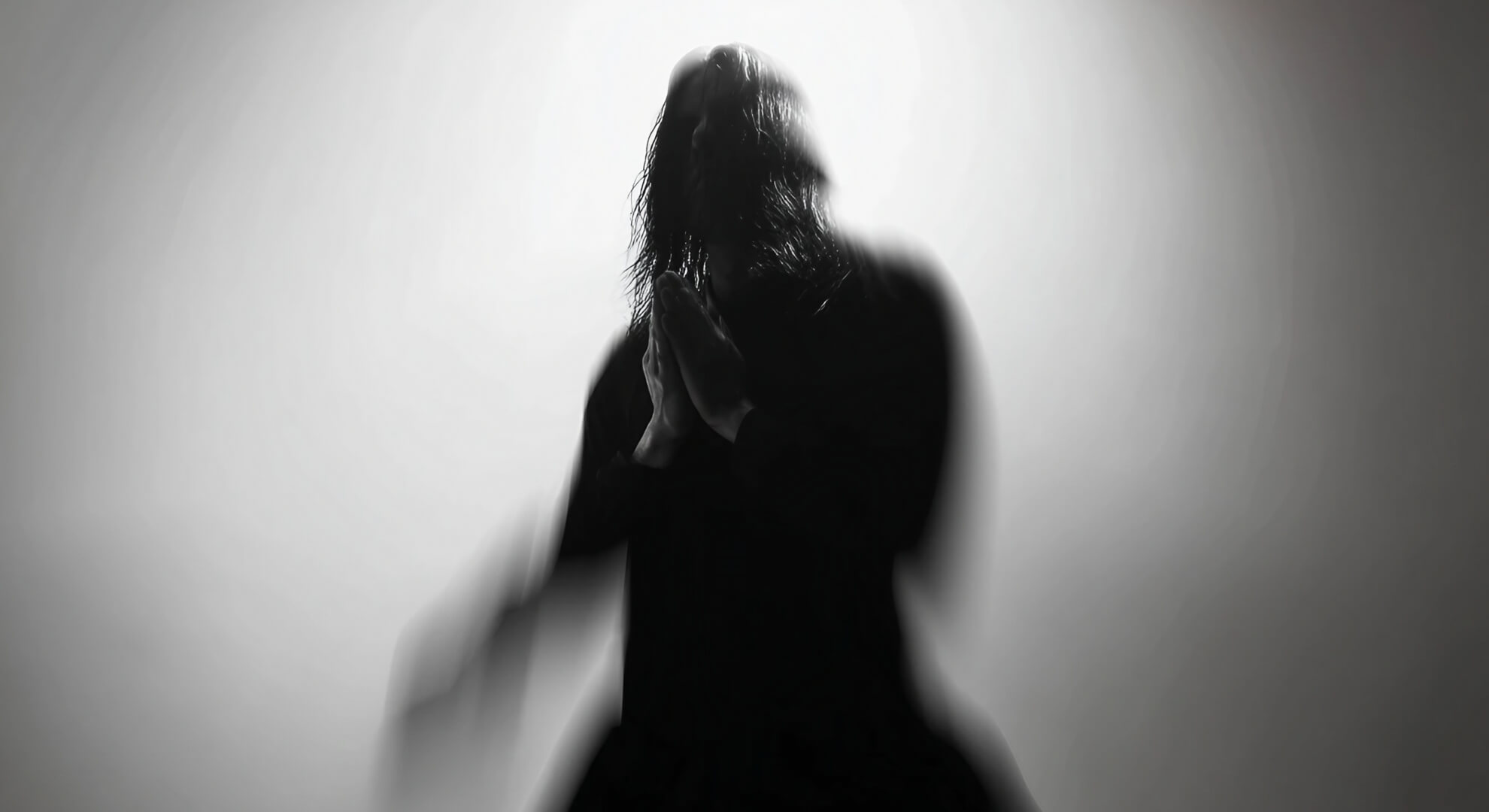 Black and white photograph of a silhouetted figure with long dark, creating an anonymous, ghostly presence.