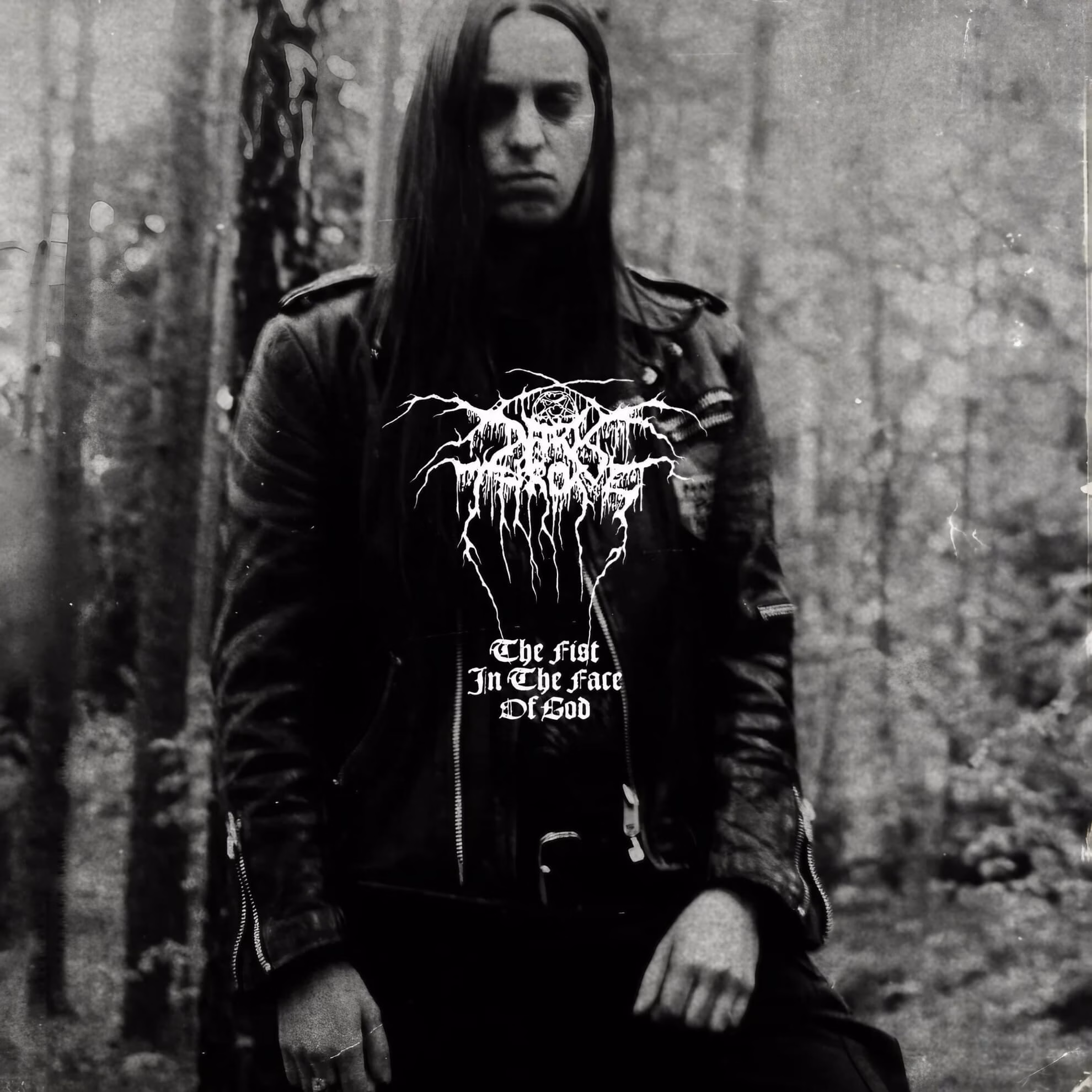 Album cover for &lsquo;The Fist in the Face of God.&rsquo; A man in a leather jacket stands before a forest backdrop, with the band&rsquo;s logo and title overlay.