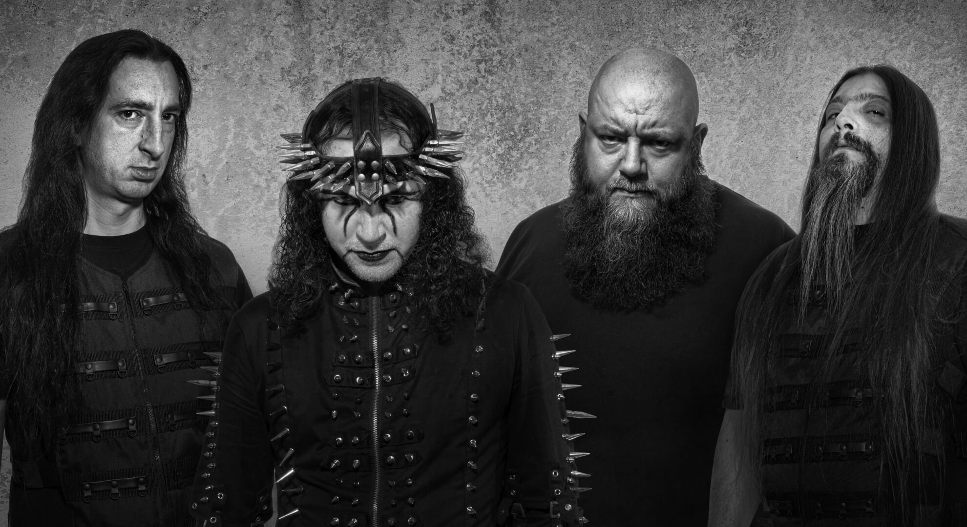 Ancient Consecrates Capital Live Concerts in Bogotá This May Four members of Ancient stand in a row against a grey concrete wall. The second figure from left wears a spiked crown headdress and stage costuming with metal studs; all four are dressed in black.