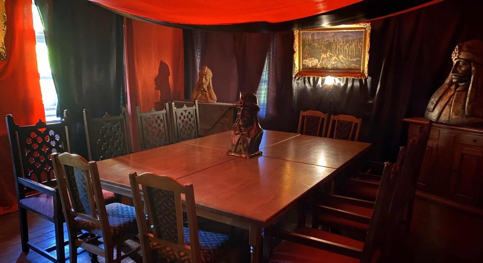 Interior of Casa Vlad Dracul restaurant, Sighișoara, with carved chairs, dining table, Vlad Tepeș busts, and red draping.