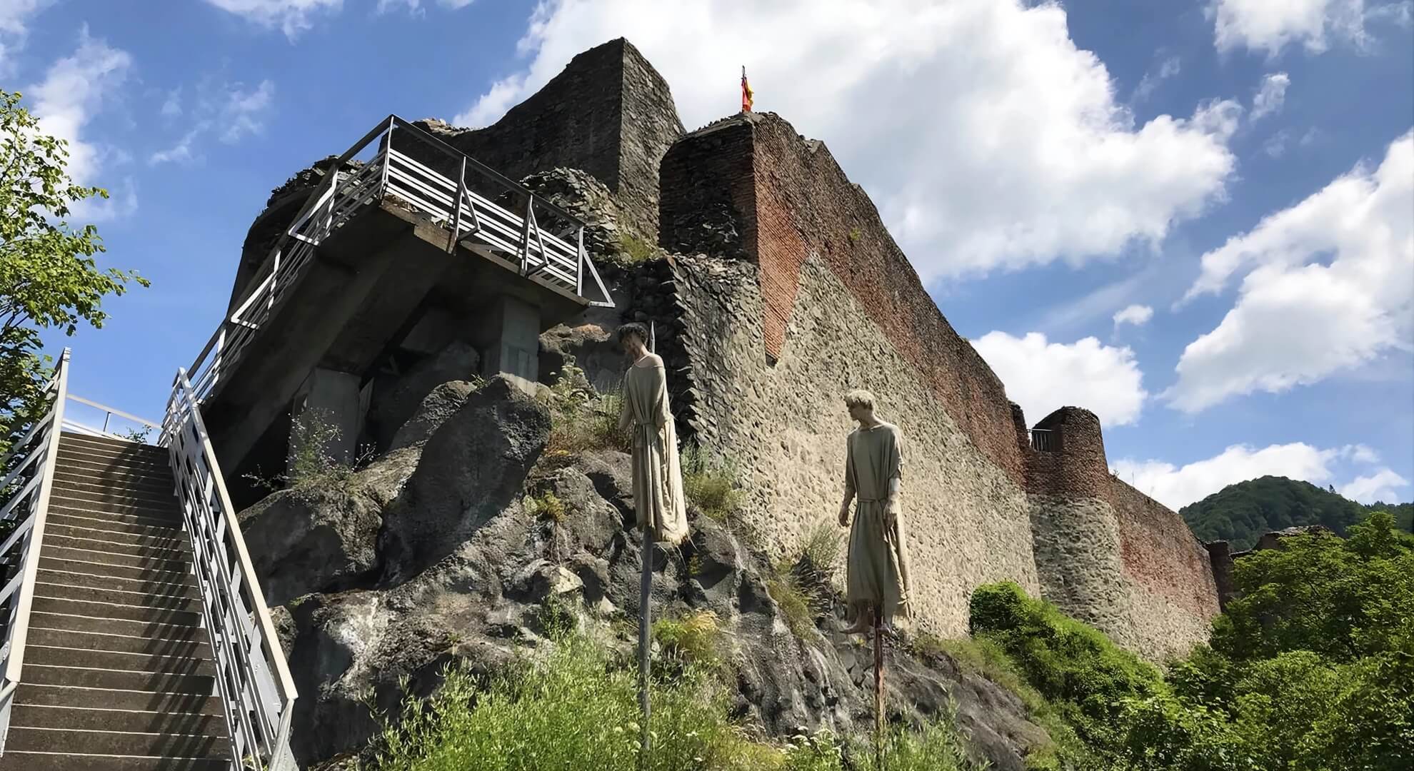Poenari Citadel ruins above the Argeș gorge, Romania, with two impalement mannequins mounted on stakes at the base of the surviving curtain wall.