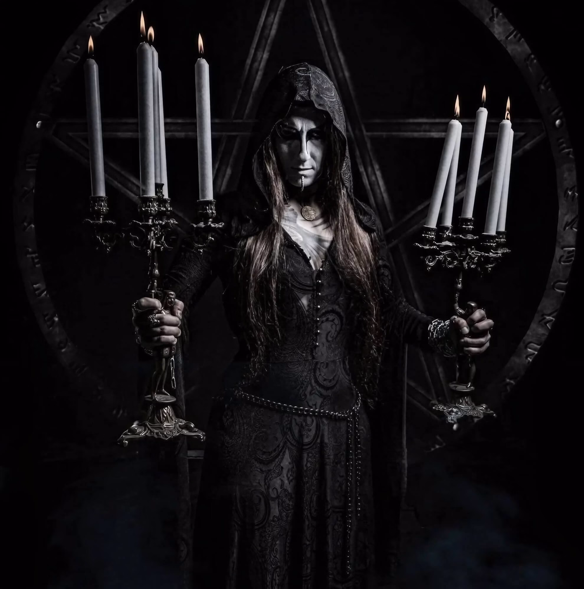 Opera IX Sharpens Its Ancient Poison on ‘Veneficium’ Dipsas Dianaria, Opera IX vocalist, holding two lit candelabras before a stone pentagram, in full corpse paint and hooded robes.