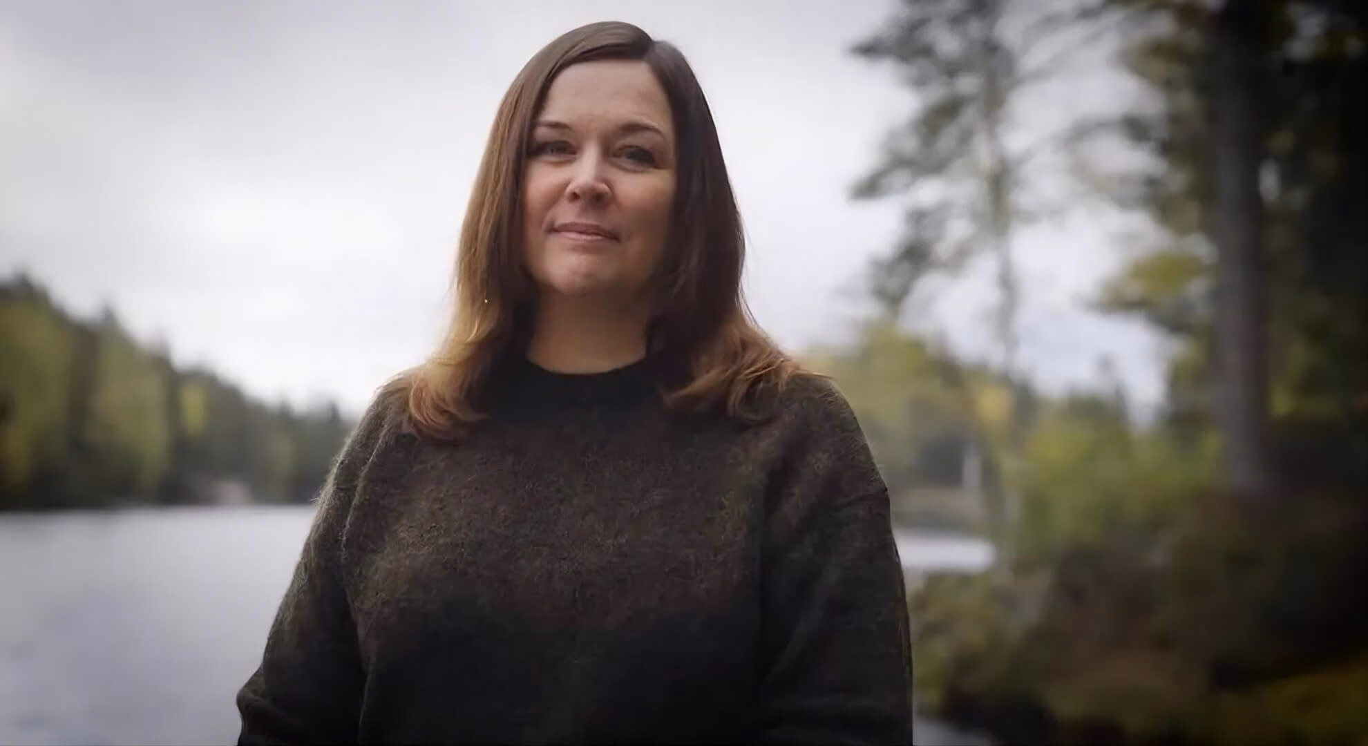 Hilde &ldquo;Hildr&rdquo; Nymoen standing outdoors before a Norwegian lake and treeline under an overcast sky.
