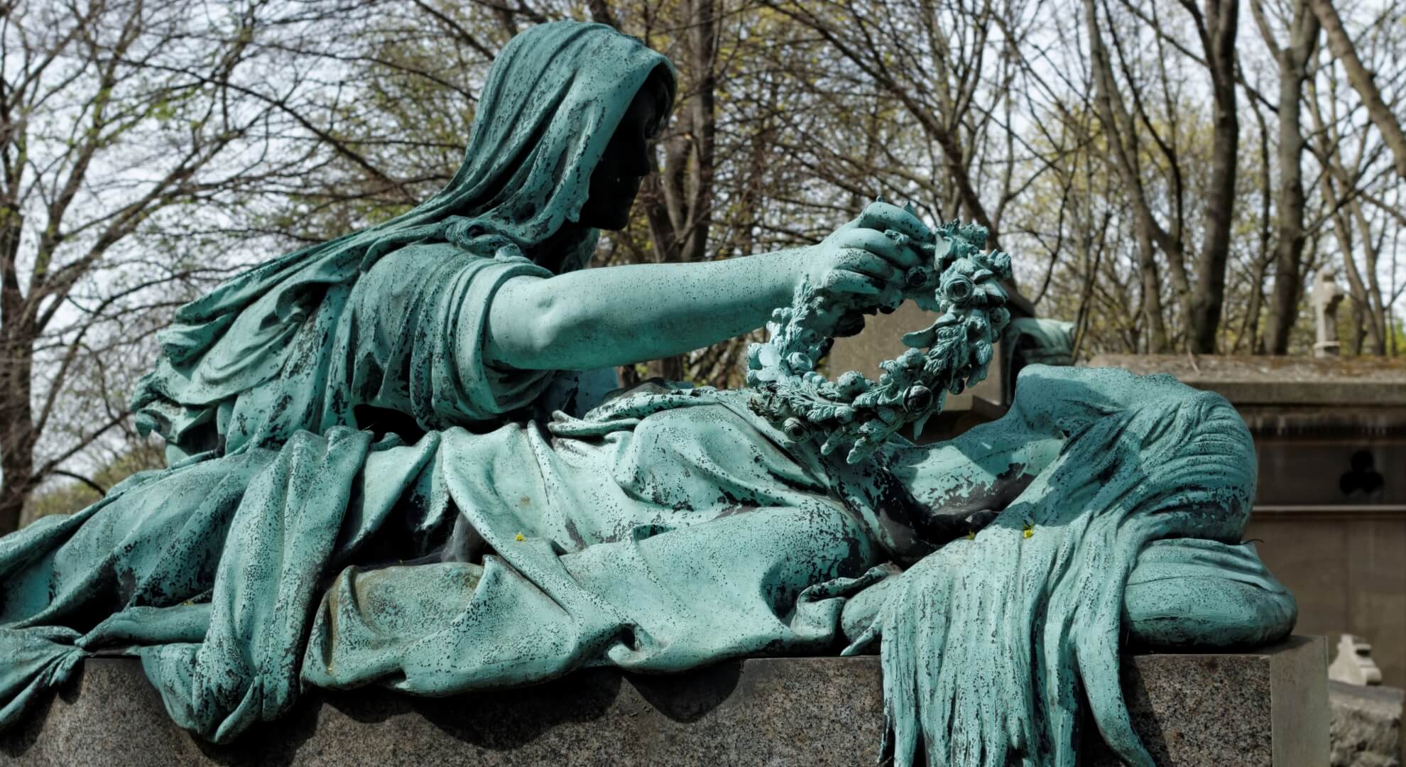 Veiled bronze figure placing a wreath on a recumbent effigy, P&egrave;re Lachaise Cemetery, Paris.