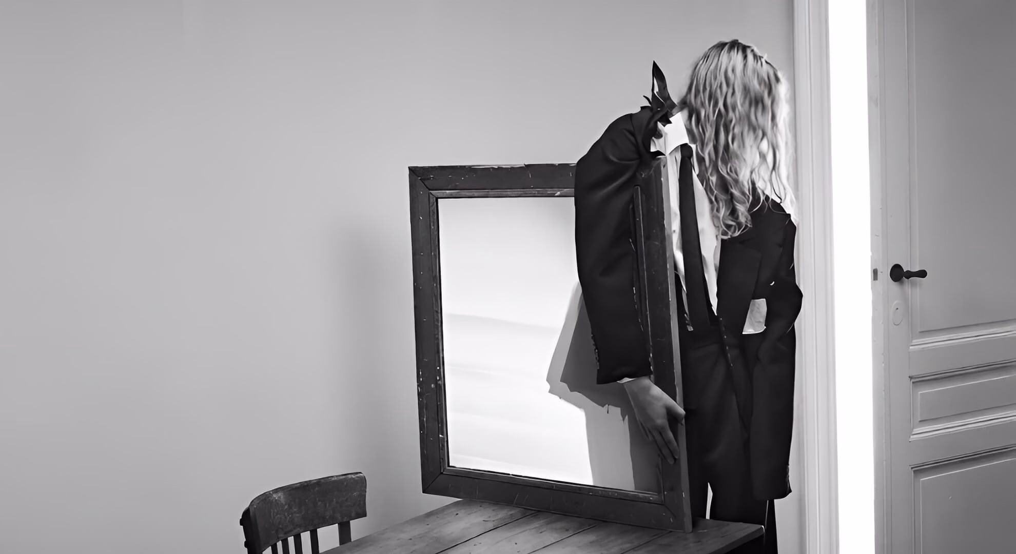 Boloria Is the First Gothic House Theyskens Did Not Inherit Boloria campaign figure in dark suit, face concealed behind a large framed mirror resting on a table.