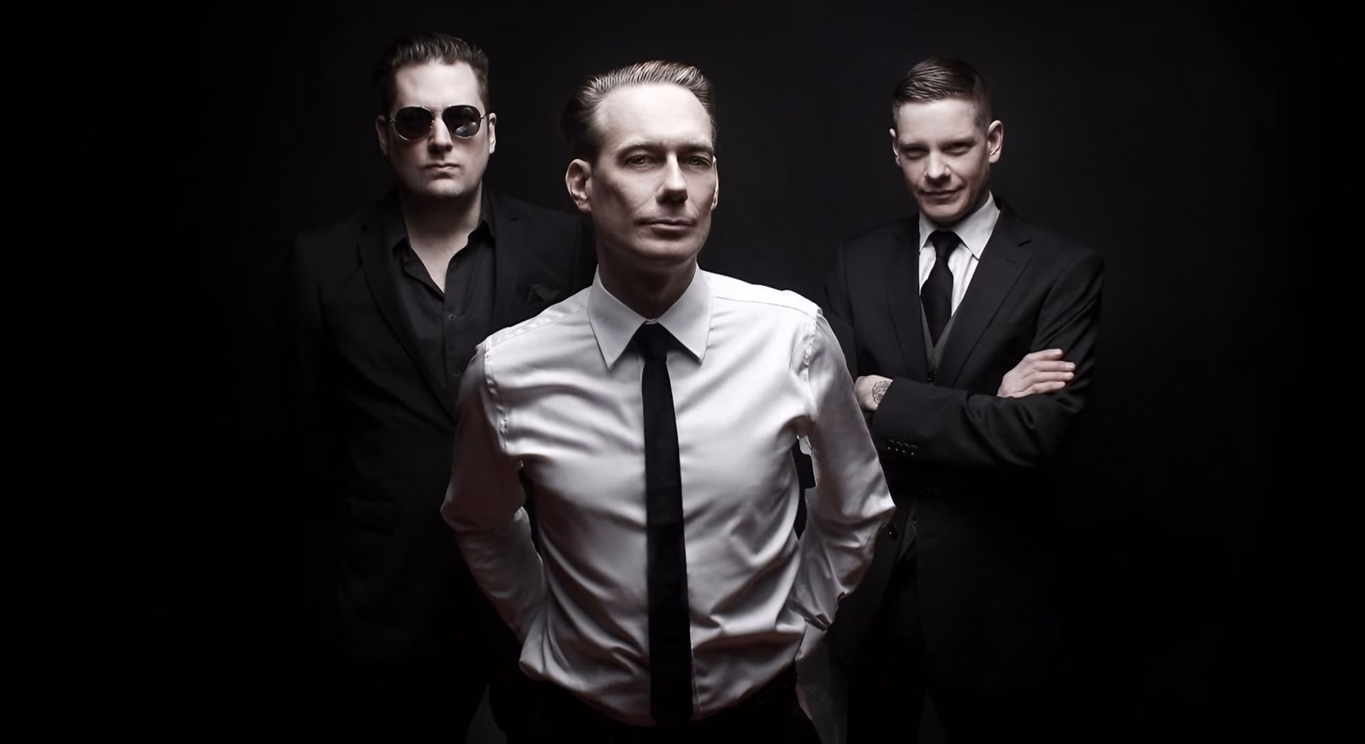 Amphi Festival Completes Two Decades on the Rhine Covenant’s three members stand in dark suits for a 2025 press photograph.