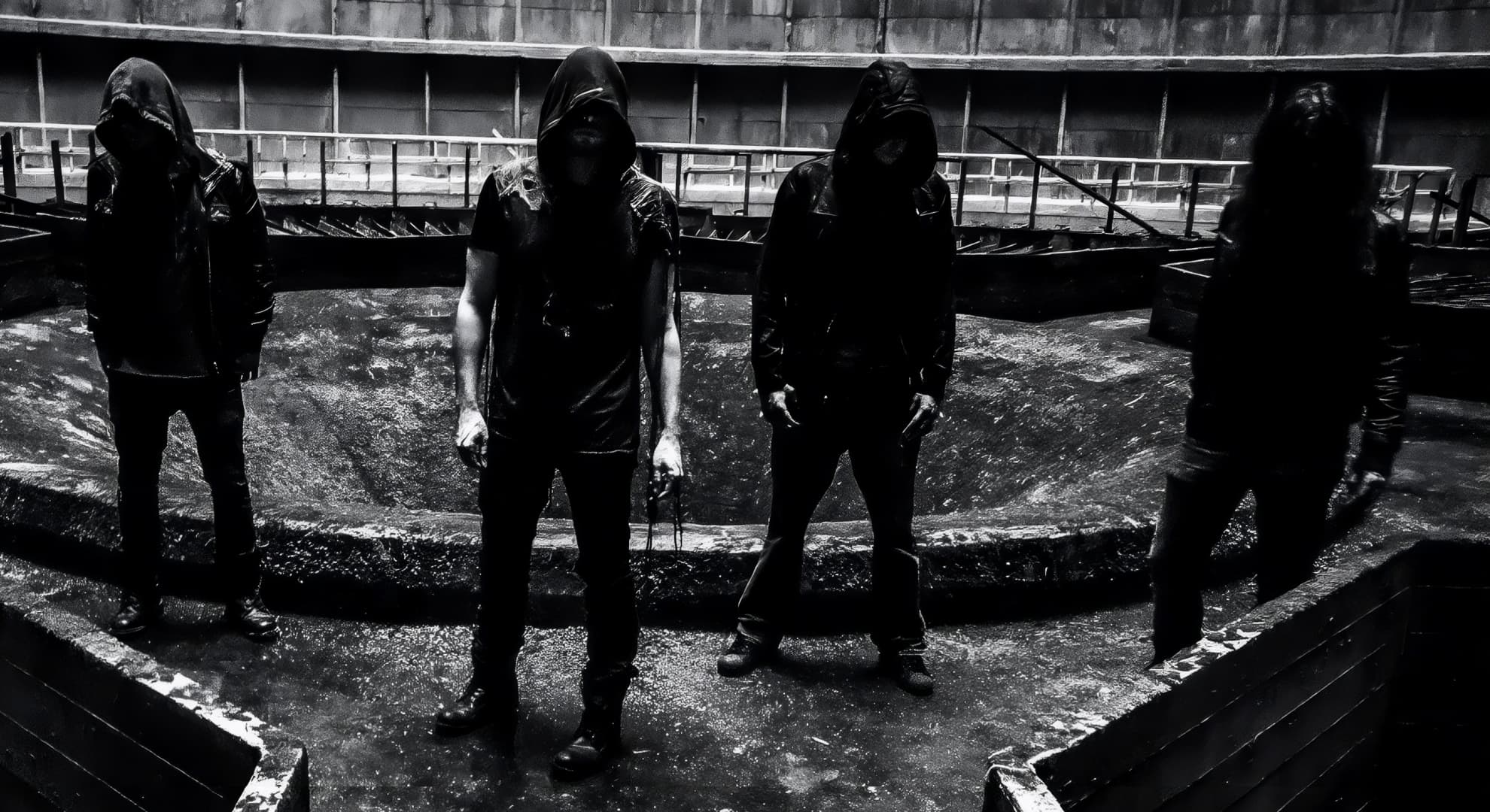 Four hooded members of Emptiness stand in a drained industrial pool, faces entirely obscured, in monochrome.