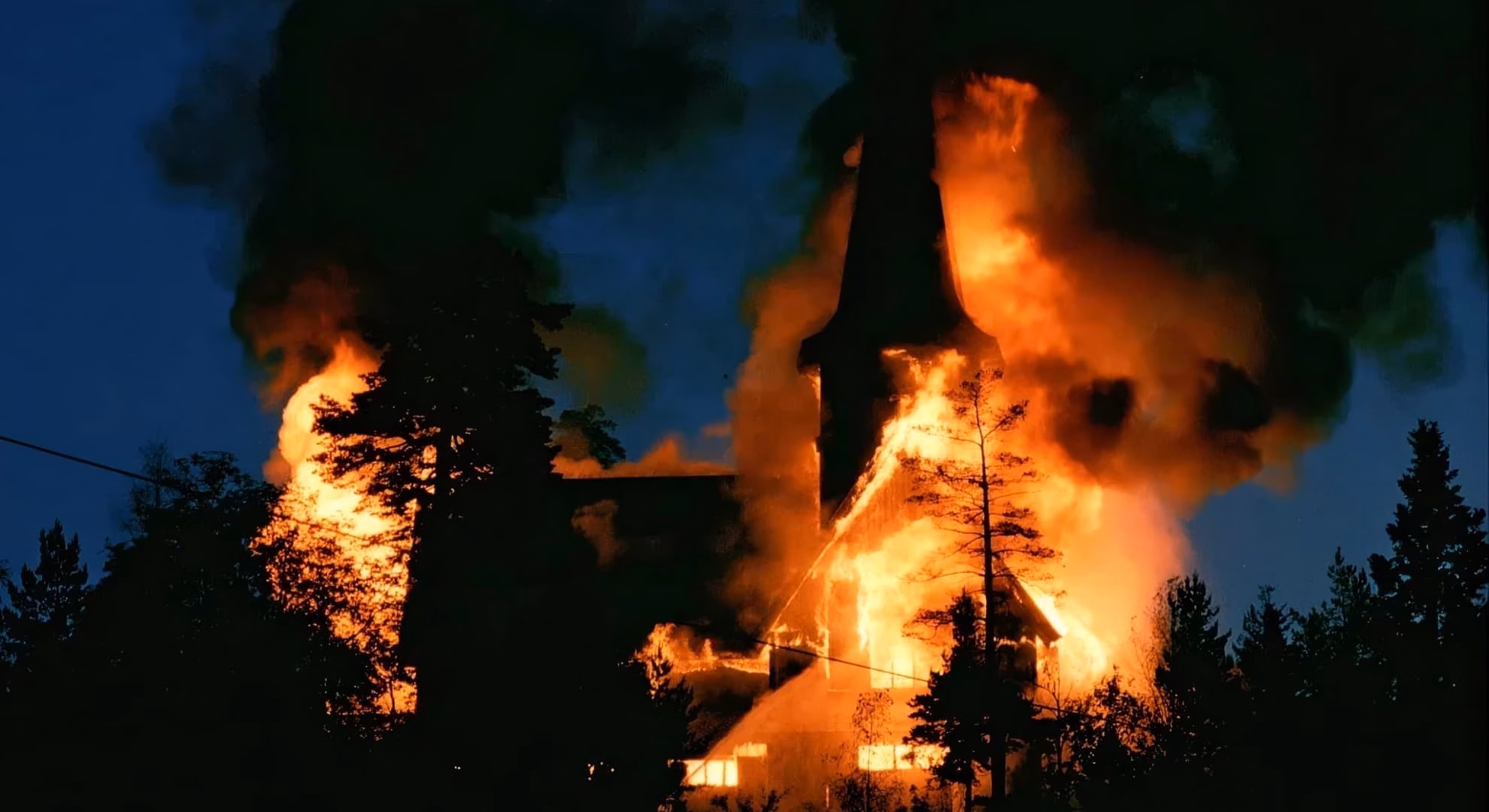 A Norwegian wooden church engulfed in flames at night, spire visible through smoke.