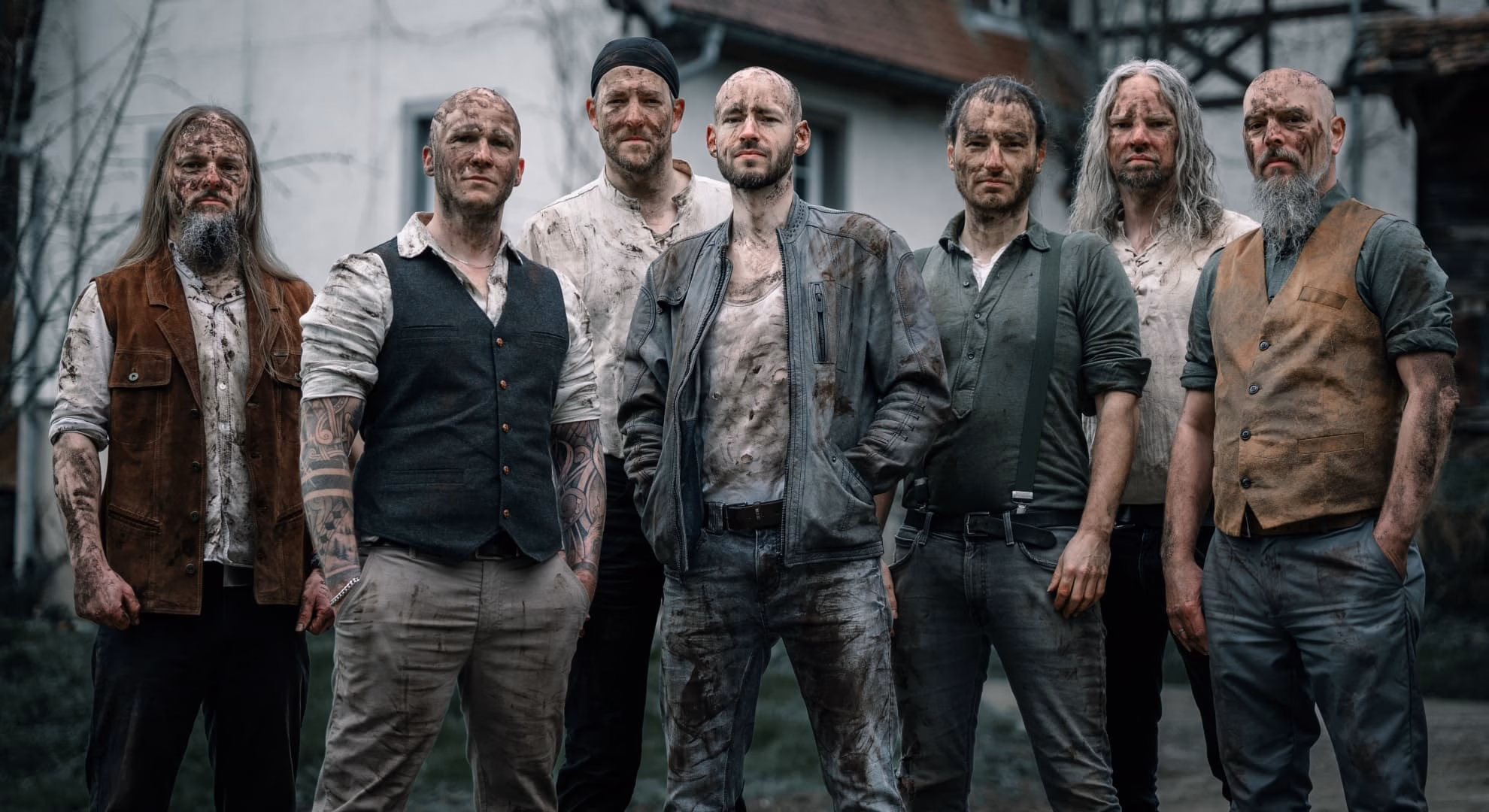 Finsterforst, seven members with soil-streaked faces, outside a half-timbered house.