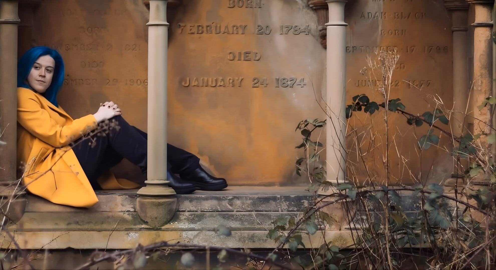 Rhiannon Grist’s ‘Home Sick’ Enters the Domestic Uncanny Rhiannon Grist, author of ‘Home Sick,’ reclining against a columned Victorian mausoleum inscribed with names and dates.