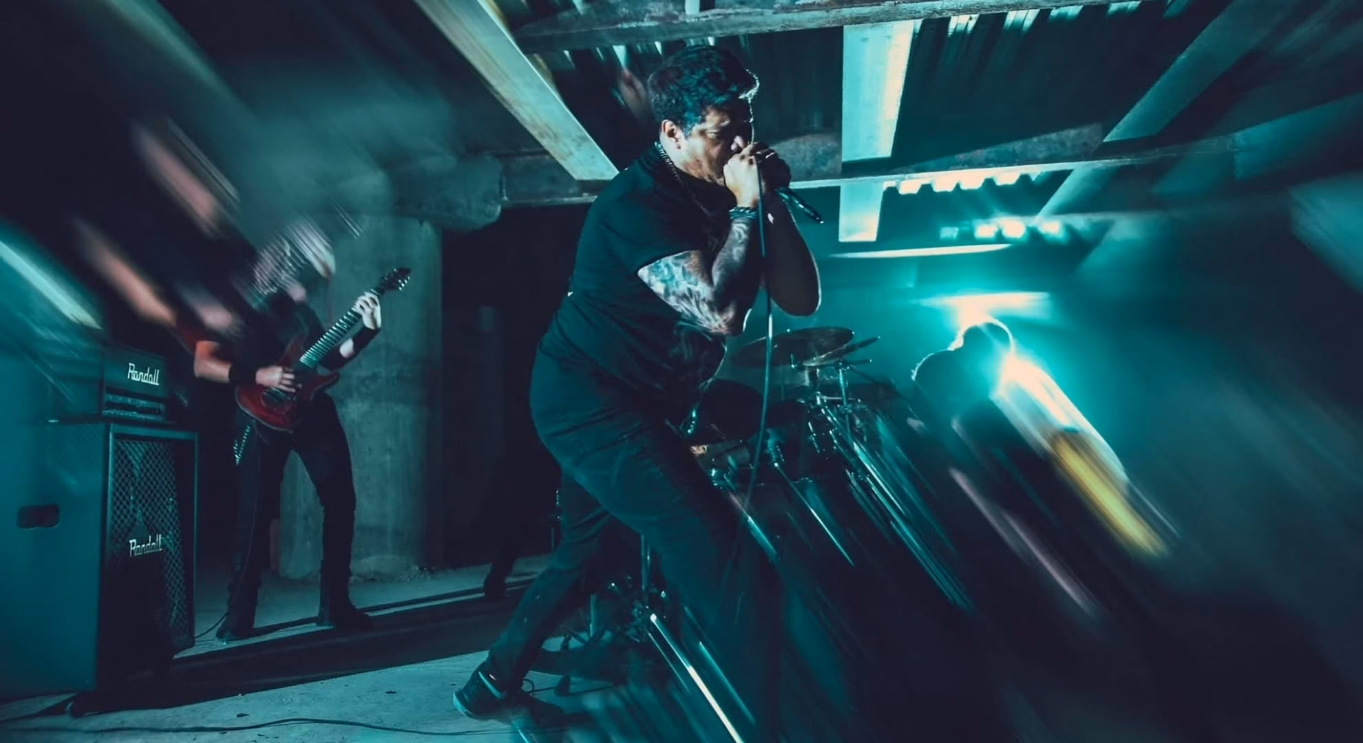 Unified Confront a ‘Devouring Plague of Mediocrity’ Hernán Chaux at the microphone under teal light in a concrete underpass, a guitarist blurred behind him.