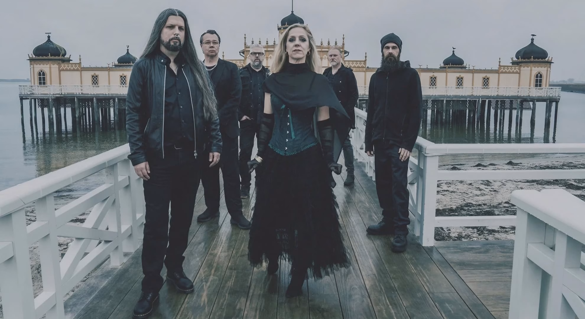 Beseech, six members in black standing in front of a Victorian pier, Sweden, 2026. (Credit: Sabine van Gameren)