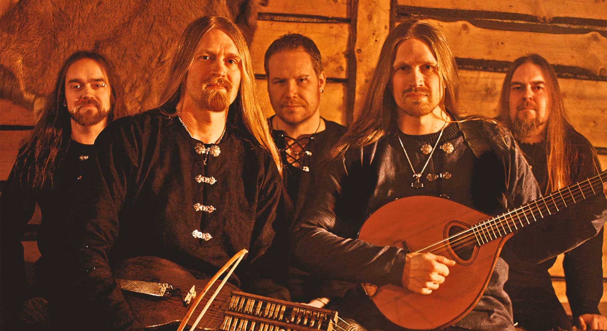 Five members of Fejd seated and standing indoors in 2021, one holding a moraharpa and bow, another a bouzouki.