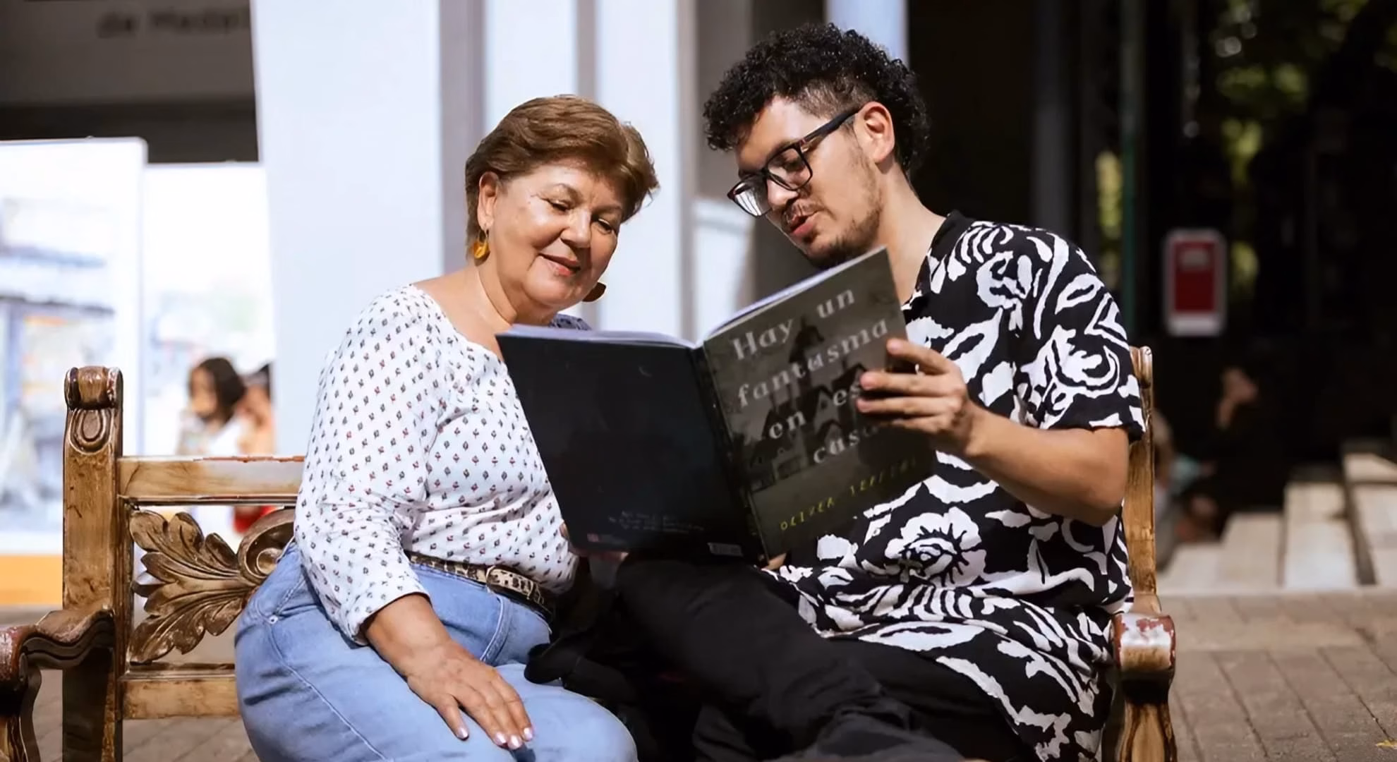 Two festival attendees reading together on a public bench during the Fiesta.