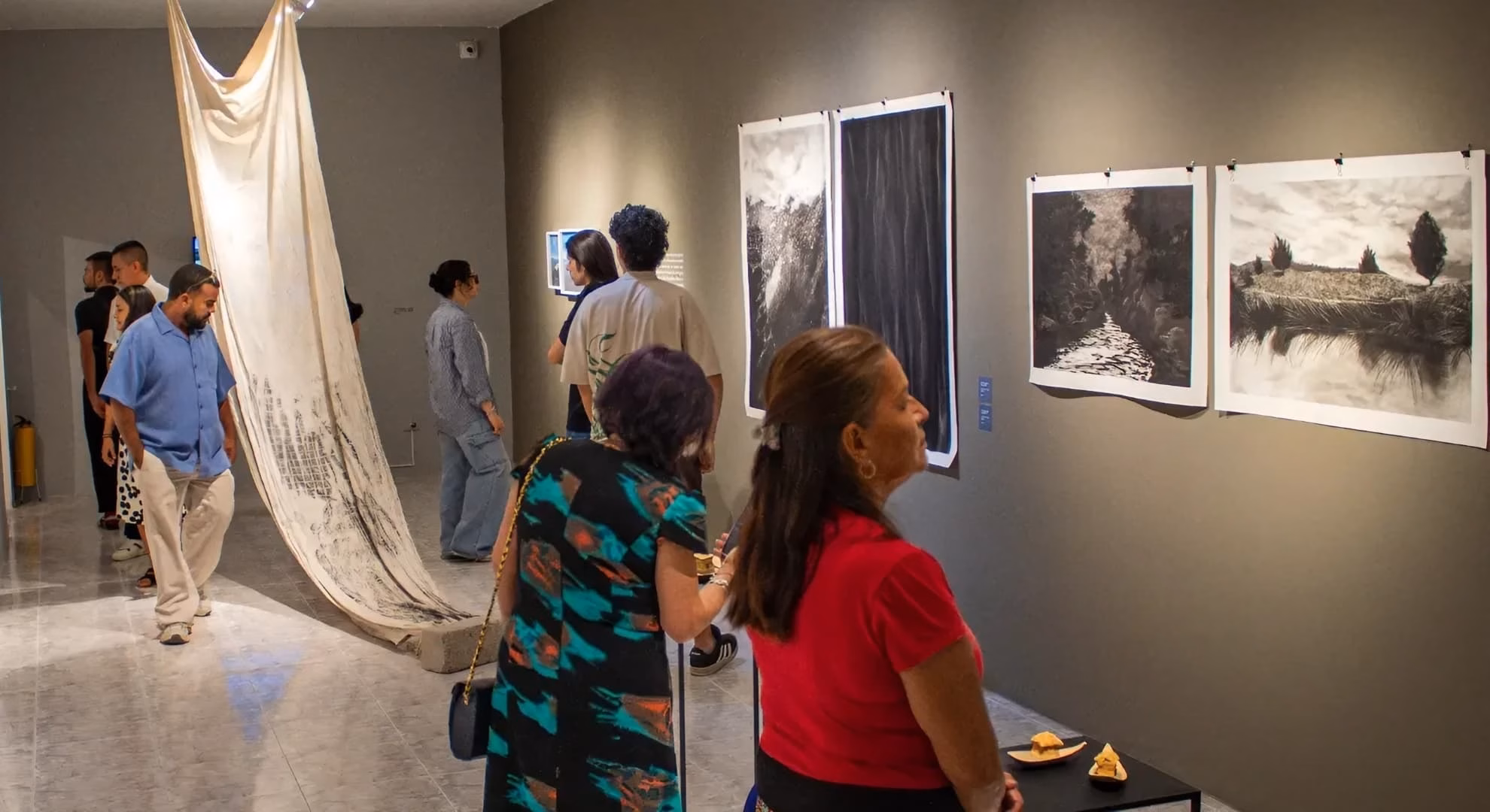 Opening-night visitors view charcoal landscape works in MAT’s 2026 season gallery, Ibagué.