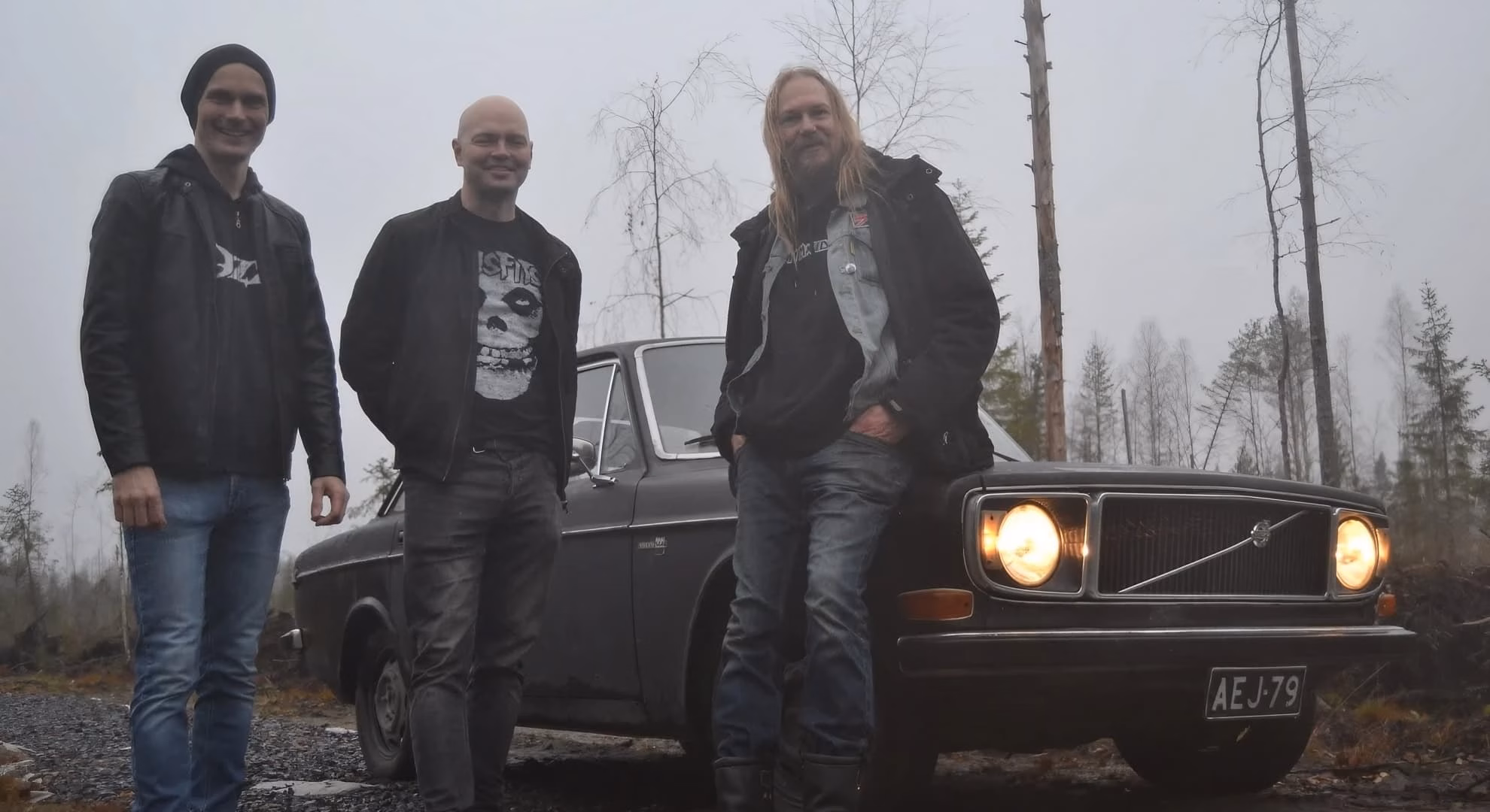 The three members of Finnish band Occult Master stand together beside a vintage sedan.