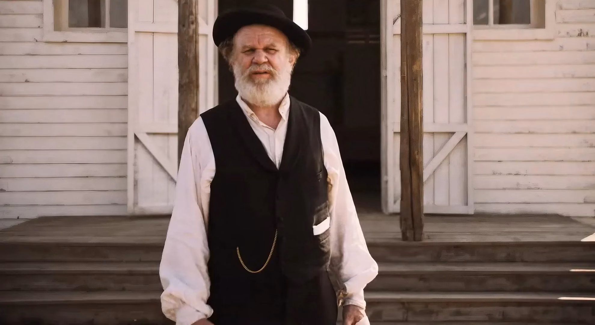 John C. Reilly as Doc standing outside a wooden building in ‘A Prayer for the Dying.’