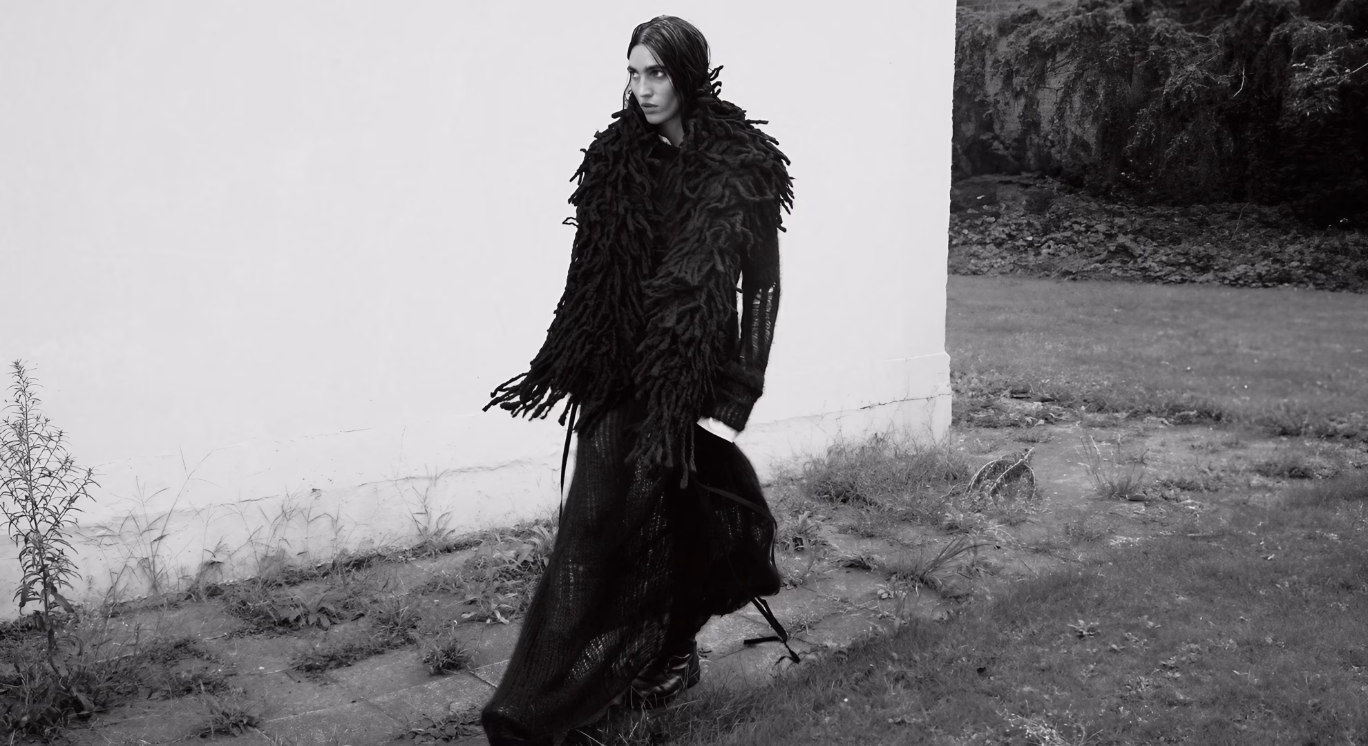 Ann Demeulemeester Carries Its Grief Into a New Century Betsy Gaghan in a floor-length black open-knit dress and heavy fringed wrap, Ann Demeulemeester Fall/Winter 2026.