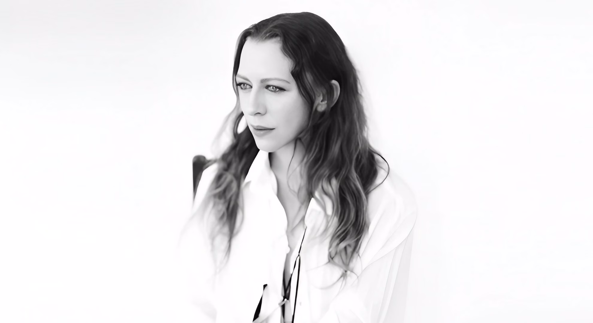 Ann Demeulemeester Carries Its Grief Into a New Century Ann Demeulemeester in a white open-collared shirt with a loose black ribbon at the neck, black-and-white portrait.