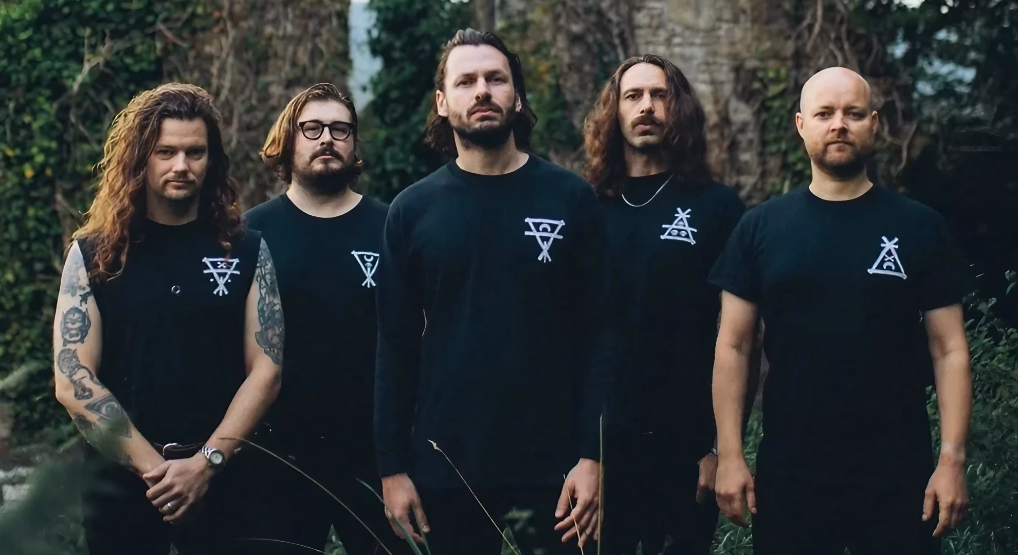 Green Lung, a five-piece band, stand together outdoors wearing matching black sigil-printed shirts.