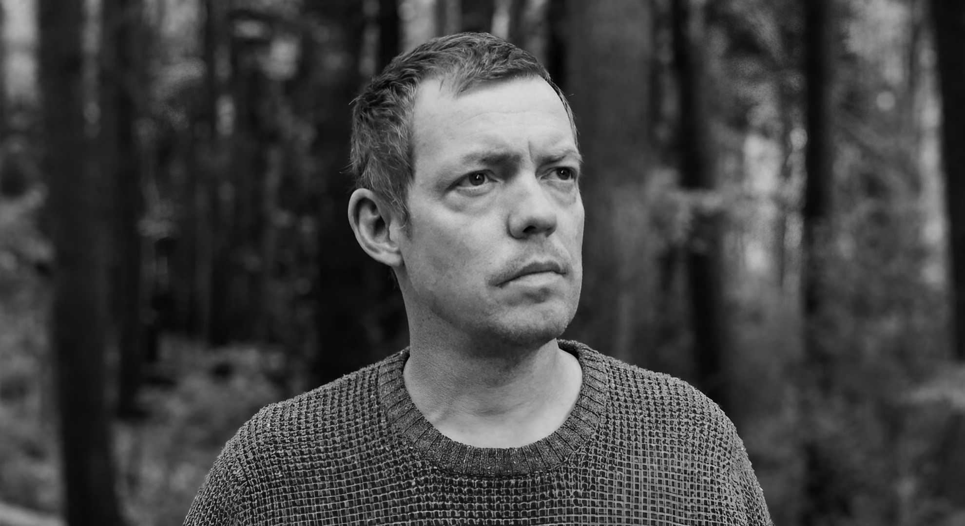 Michael Wehunt, author of ‘Nightjars,’ looking away from the camera among tall tree trunks.