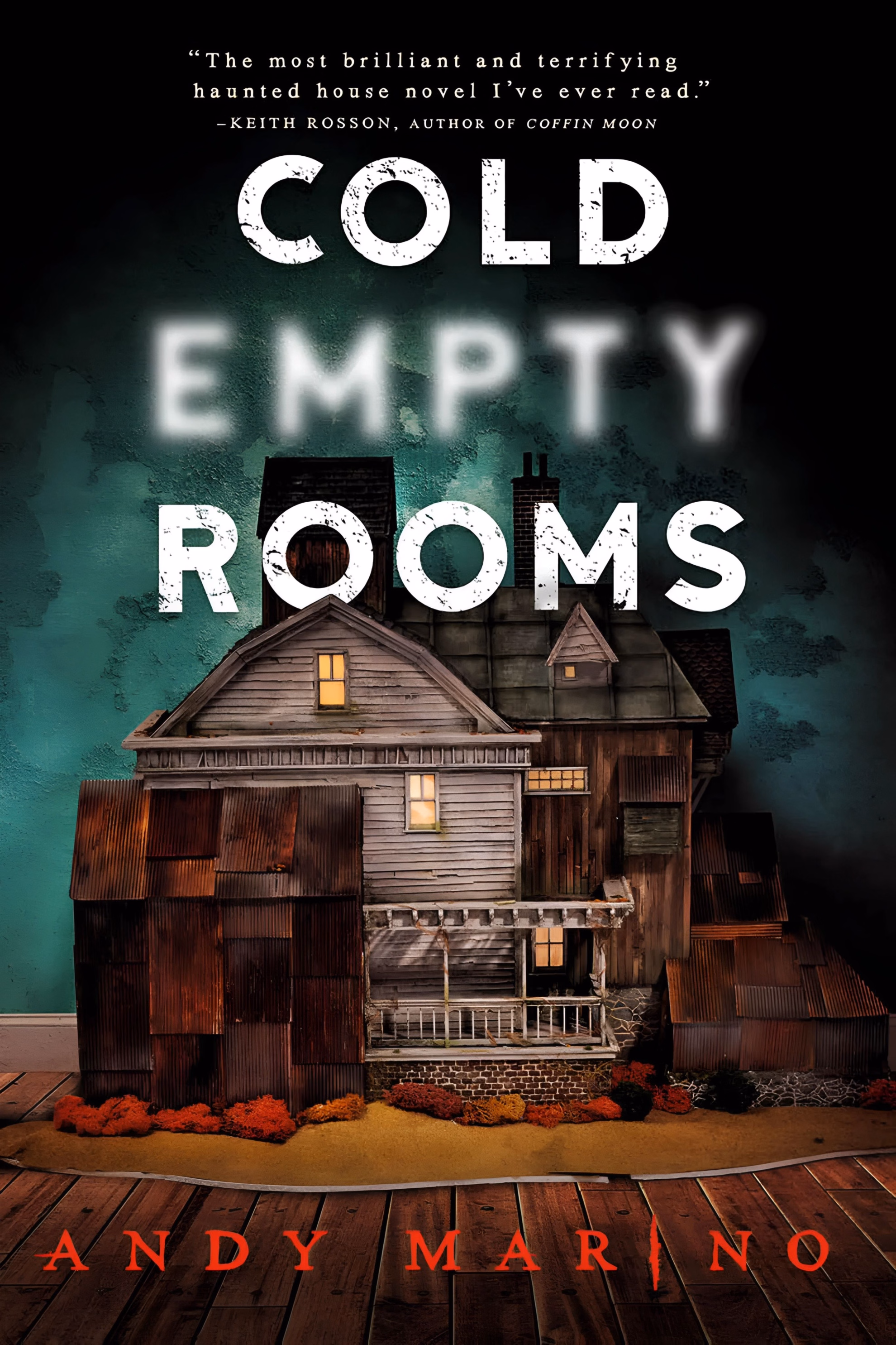 Book cover of ‘Cold Empty Rooms’ by Andy Marino. A photographed model house with lit windows stands on a wooden floor against a teal wall.